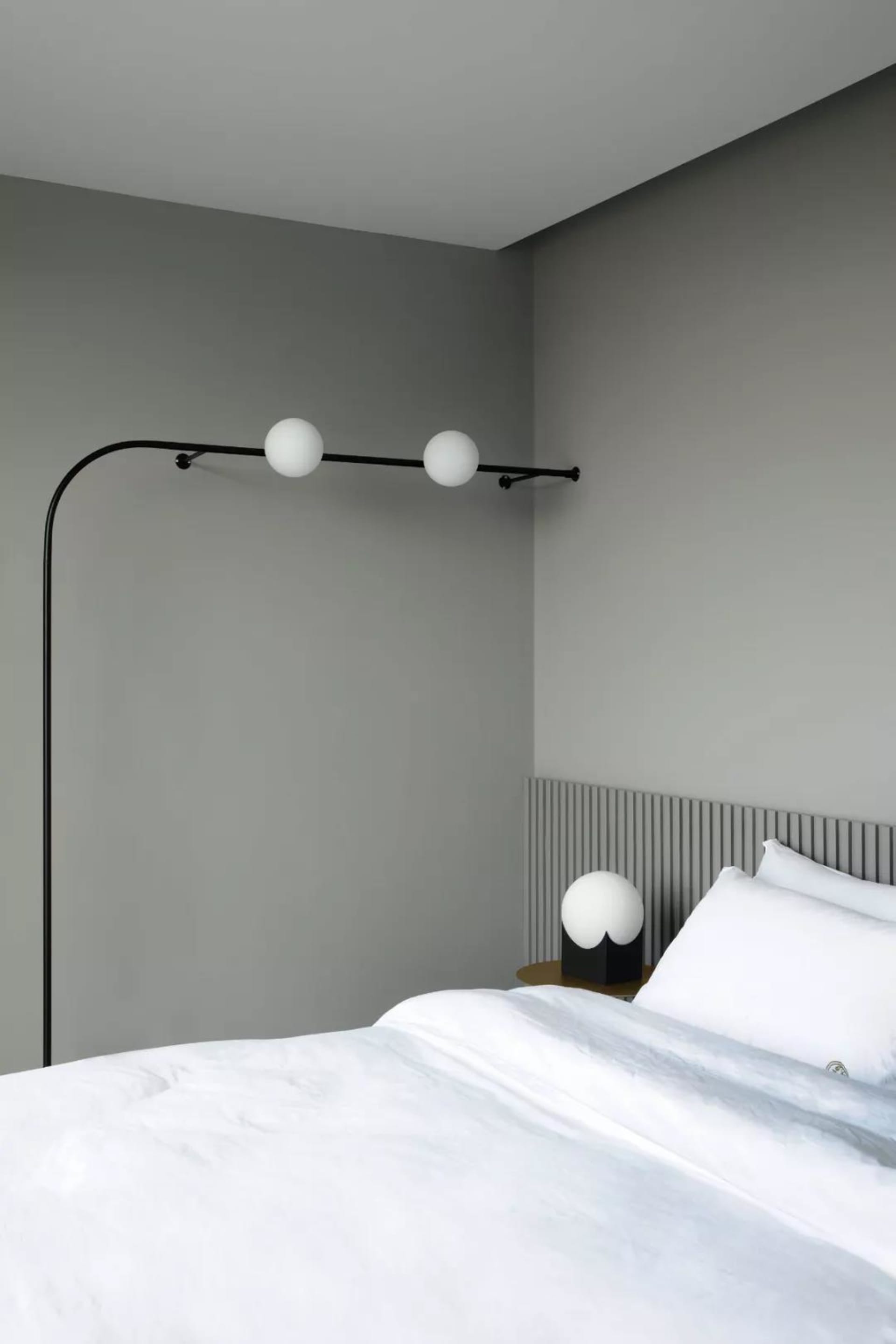 A minimalist bedroom with a white bed, lamp, and grey walls.