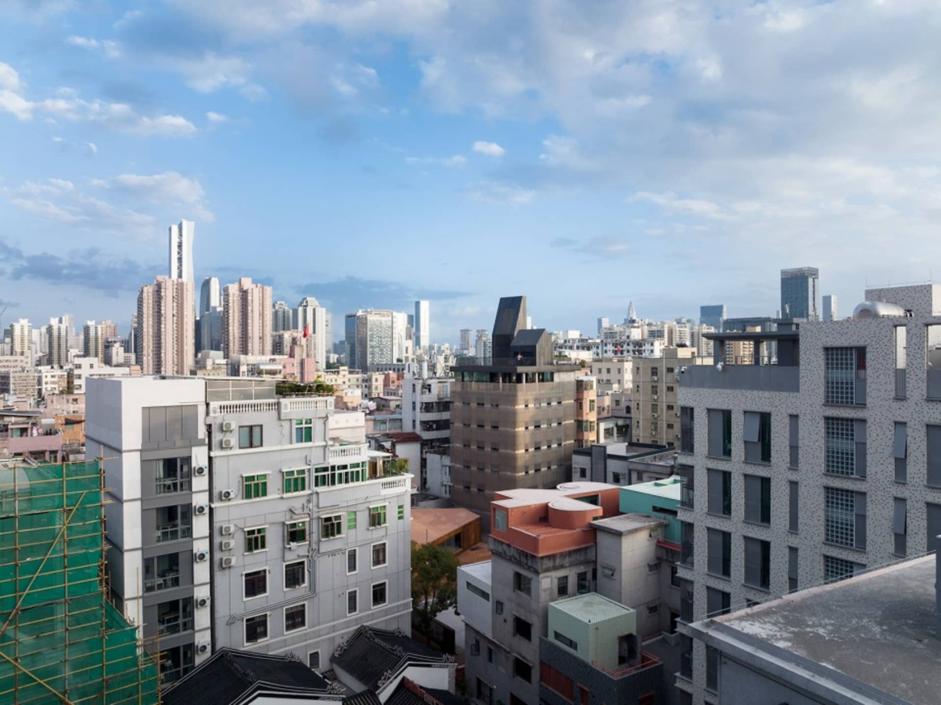 現代都市景觀，混凝土、玻璃與鋼材建築矗立於多雲的天空下。