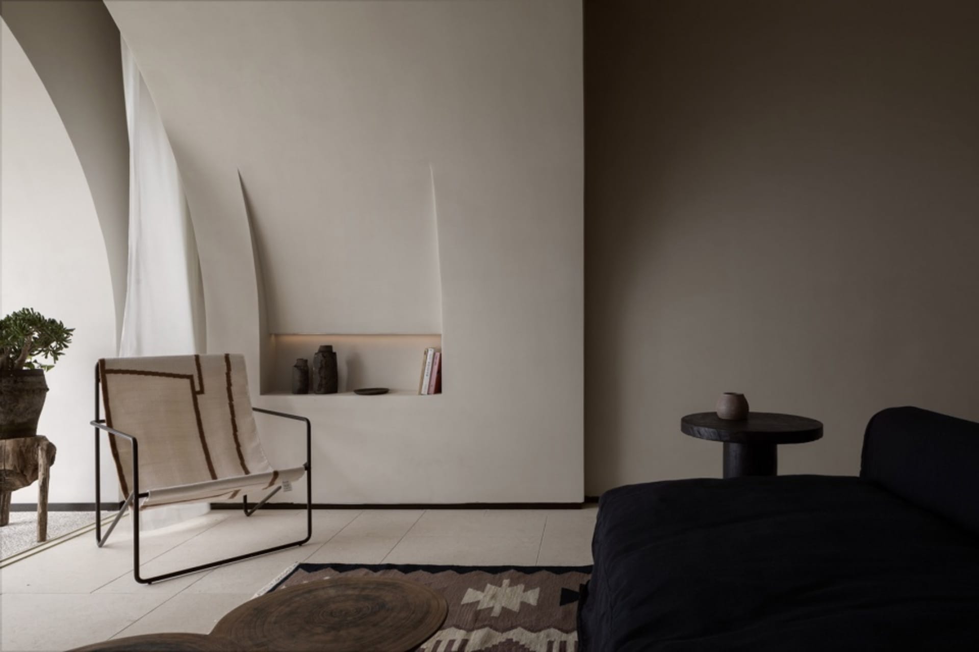 Minimalist living room with concrete walls, a black sofa, and a woven chair.