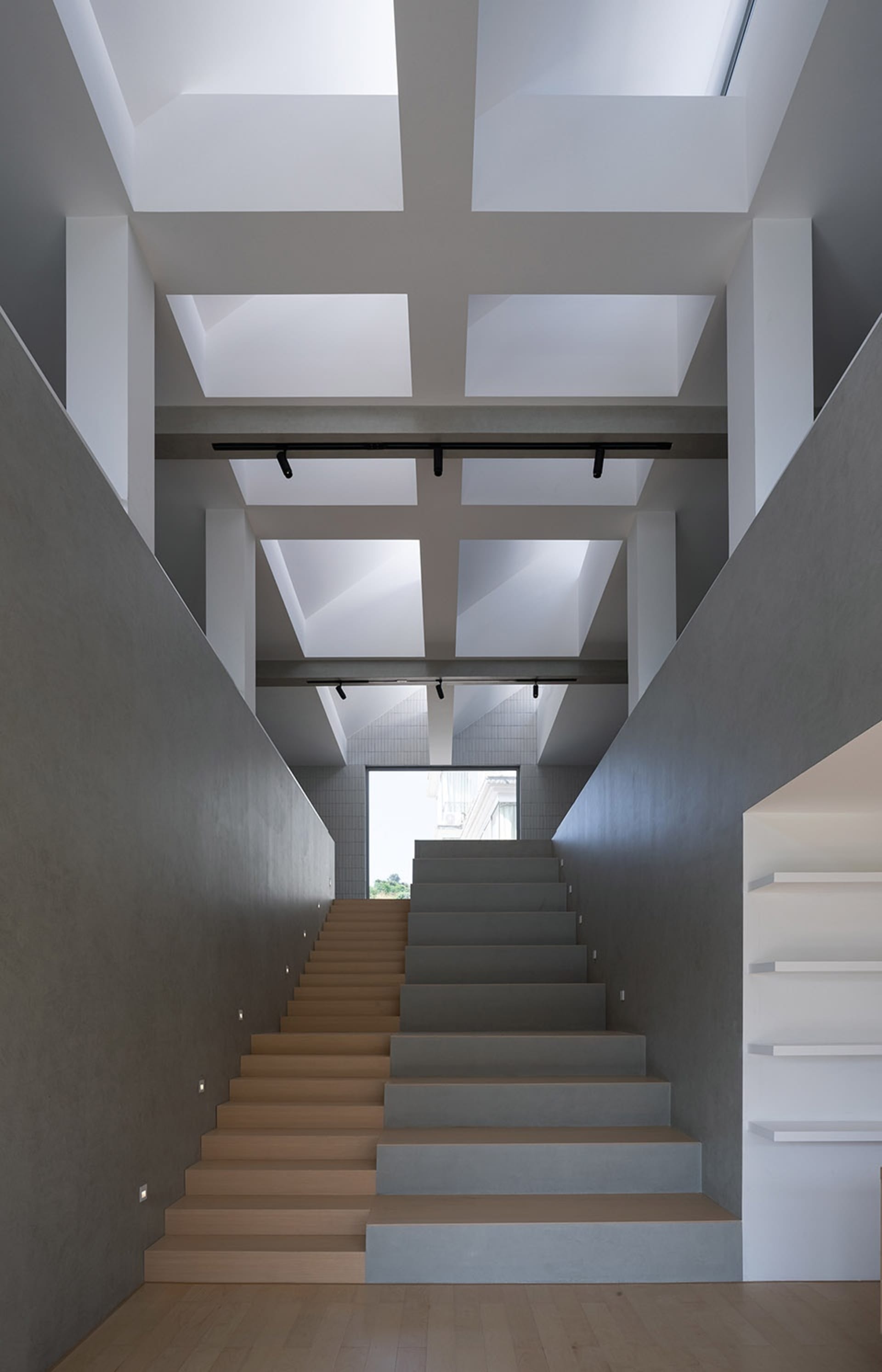 Modern staircase with concrete steps and wooden treads, featuring a minimalist design with exposed beams and skylights.