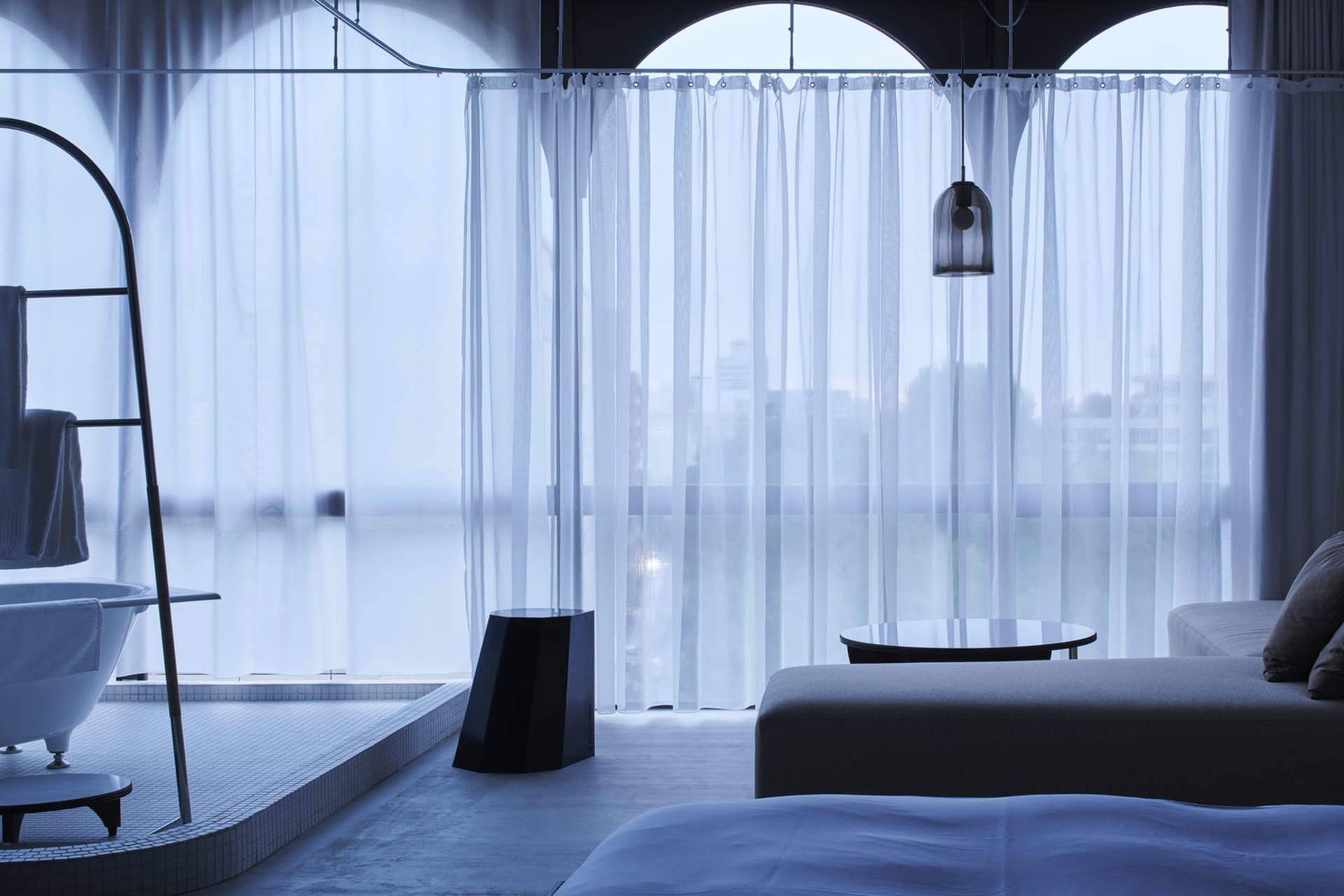 A modern residential interior with transparent curtains, glass surfaces, and minimalist furniture.
