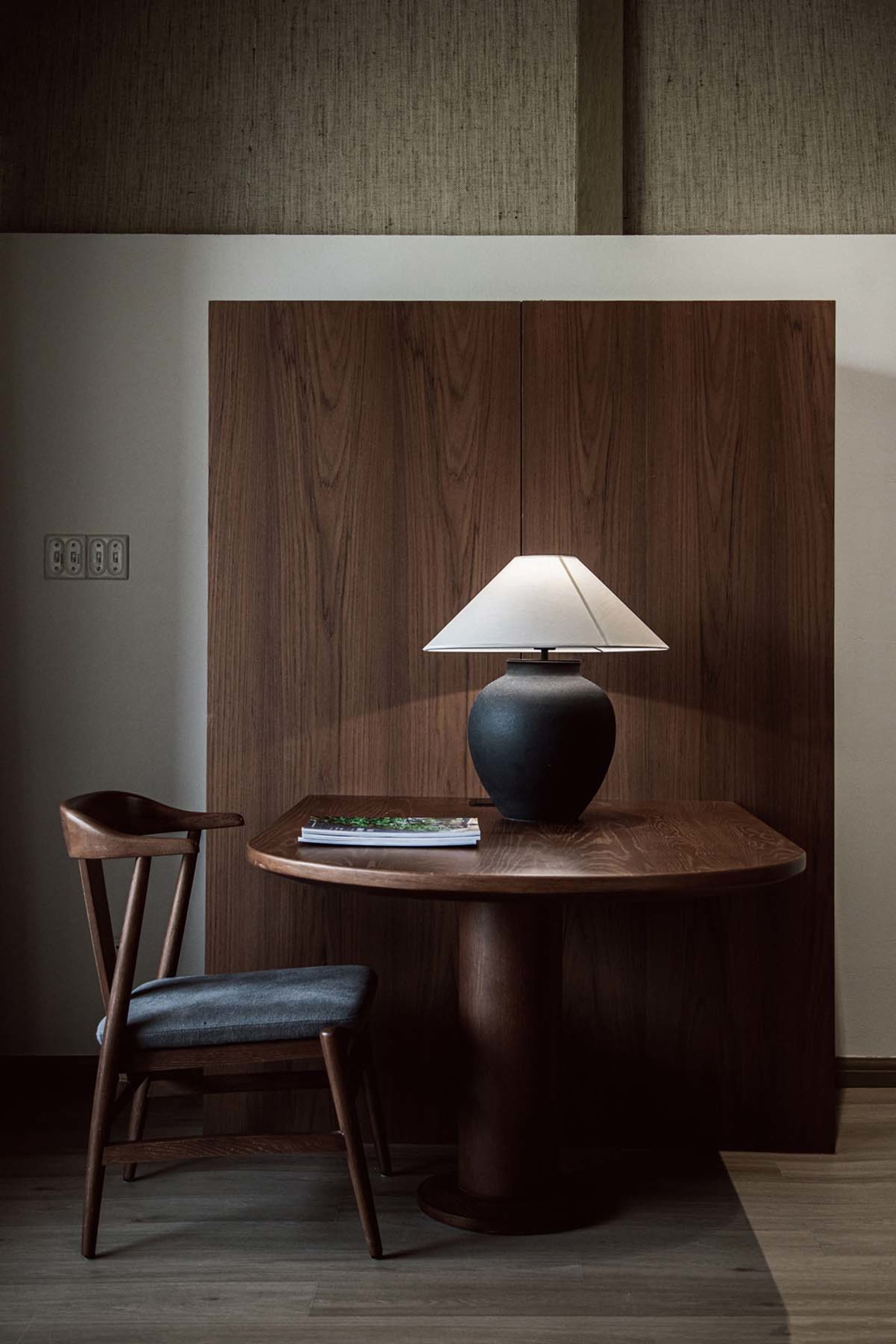 A modern home office with a wooden desk, chair, and lamp.