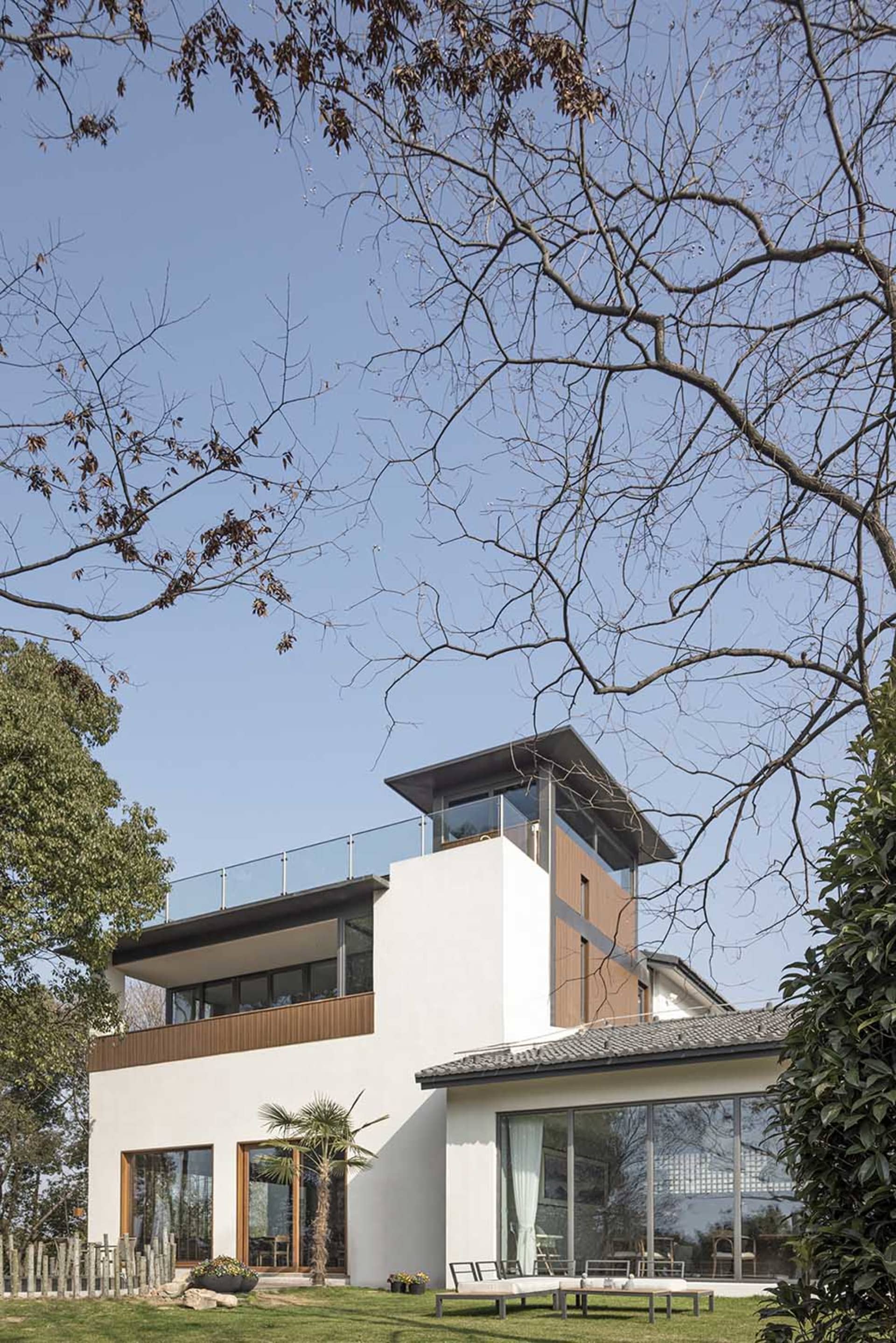 A modern house with white stucco exterior, featuring large glass windows and a rooftop deck.