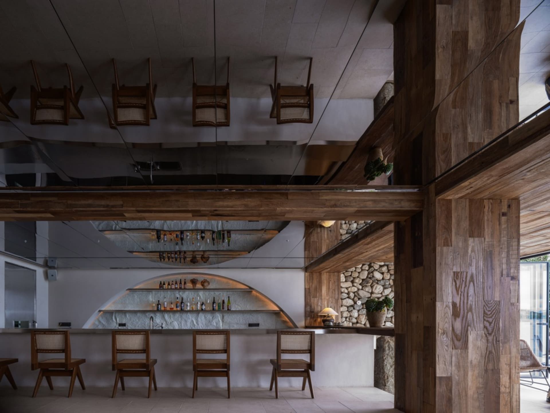 A modern restaurant bar with wooden chairs, a concrete countertop, and a rustic stone wall.