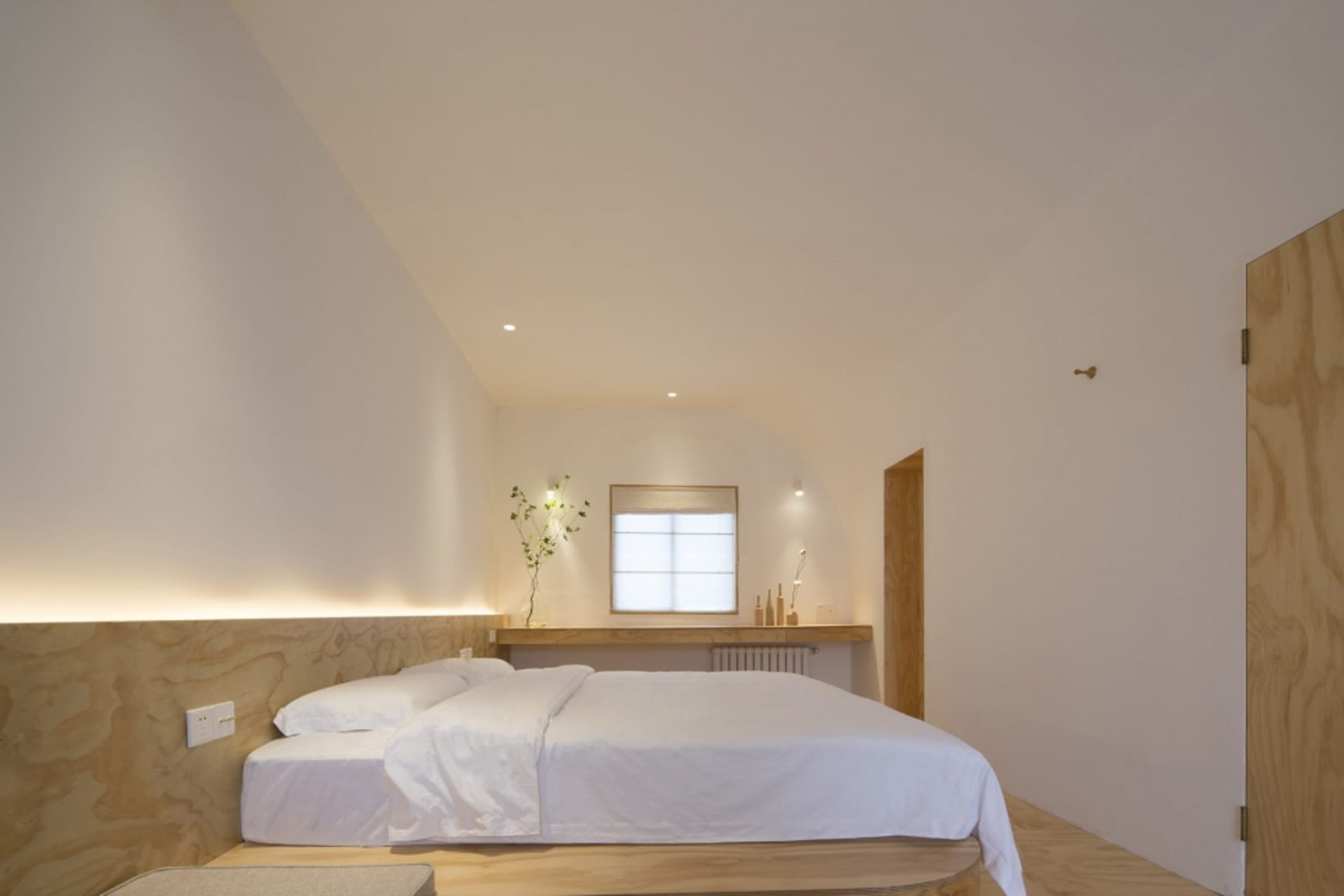 Minimalist bedroom with a white bed, wooden headboard, and minimalist decor.