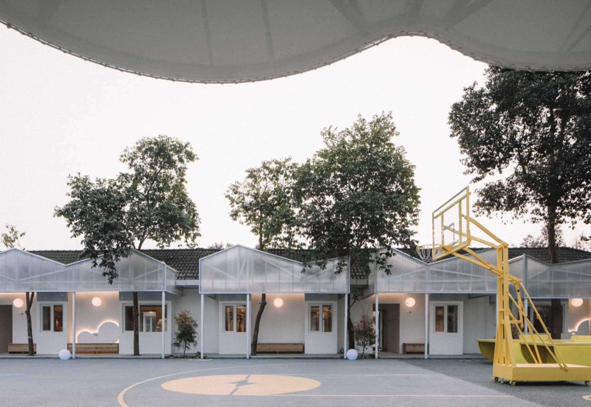 An outdoor basketball court with a glass-roofed pavilion and surrounding greenery on a clear day.