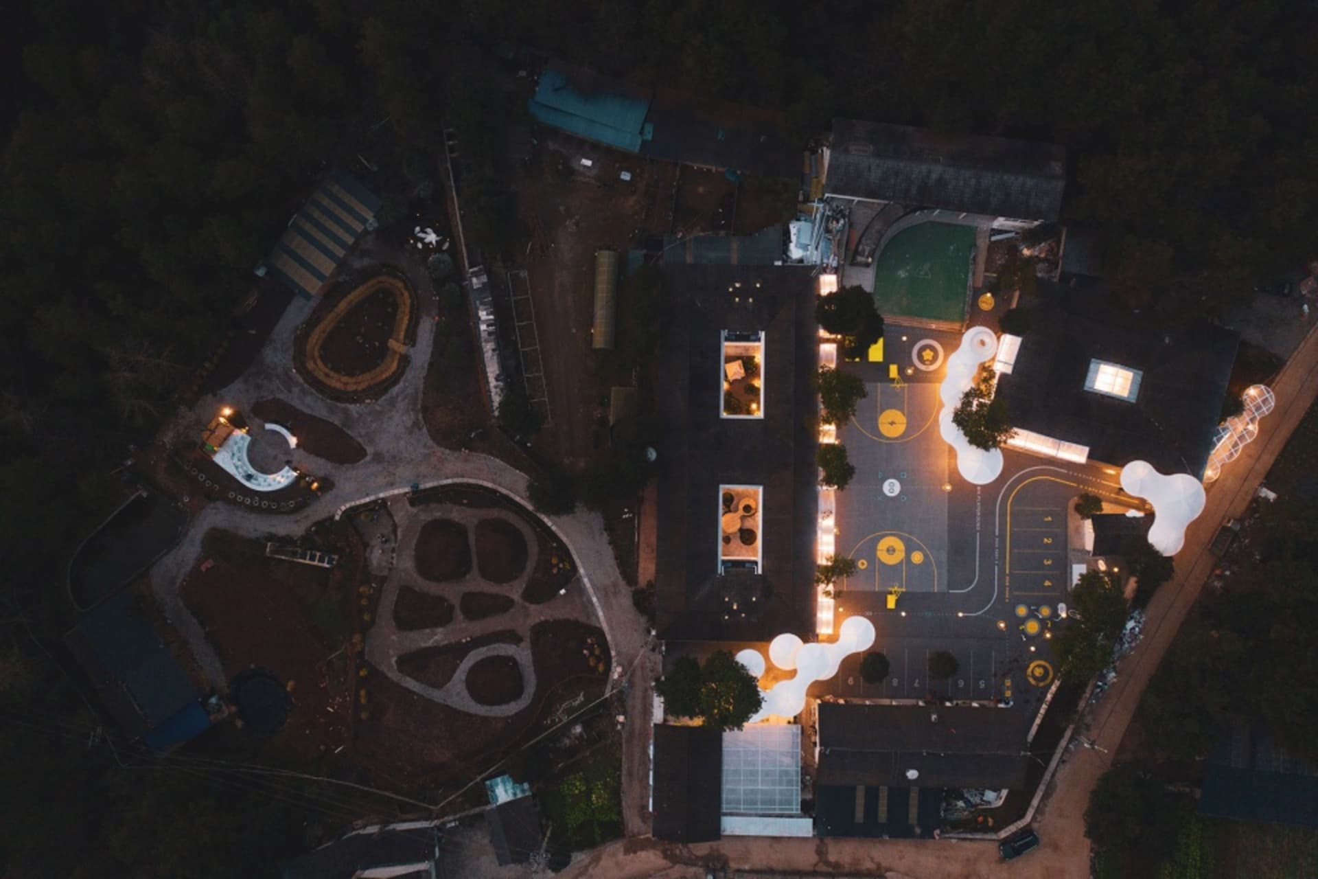 Aerial view of a school campus with various buildings, a basketball court, and a swimming pool at night.