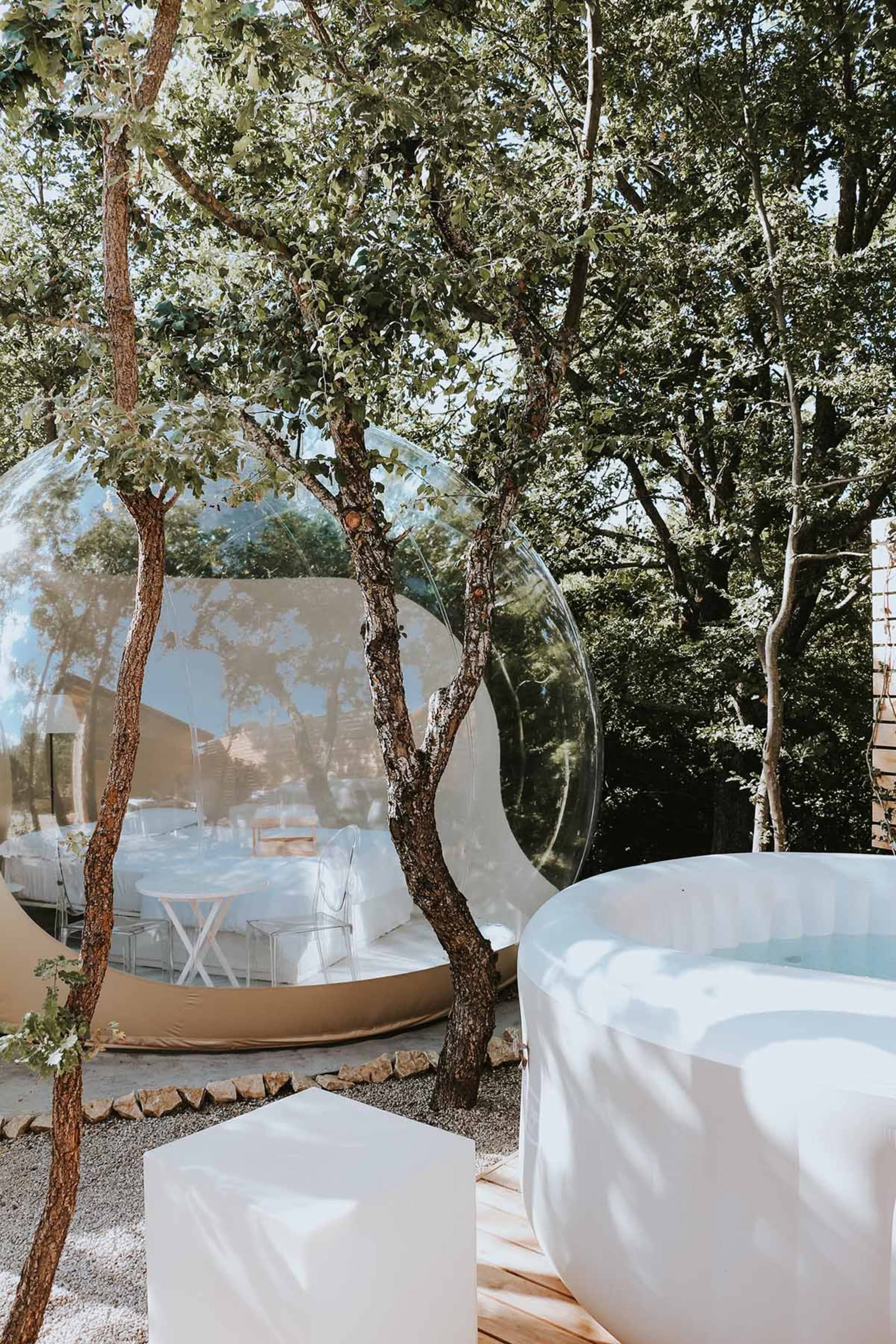 A transparent glass dome nestled among trees, featuring a white interior with a table and chairs.