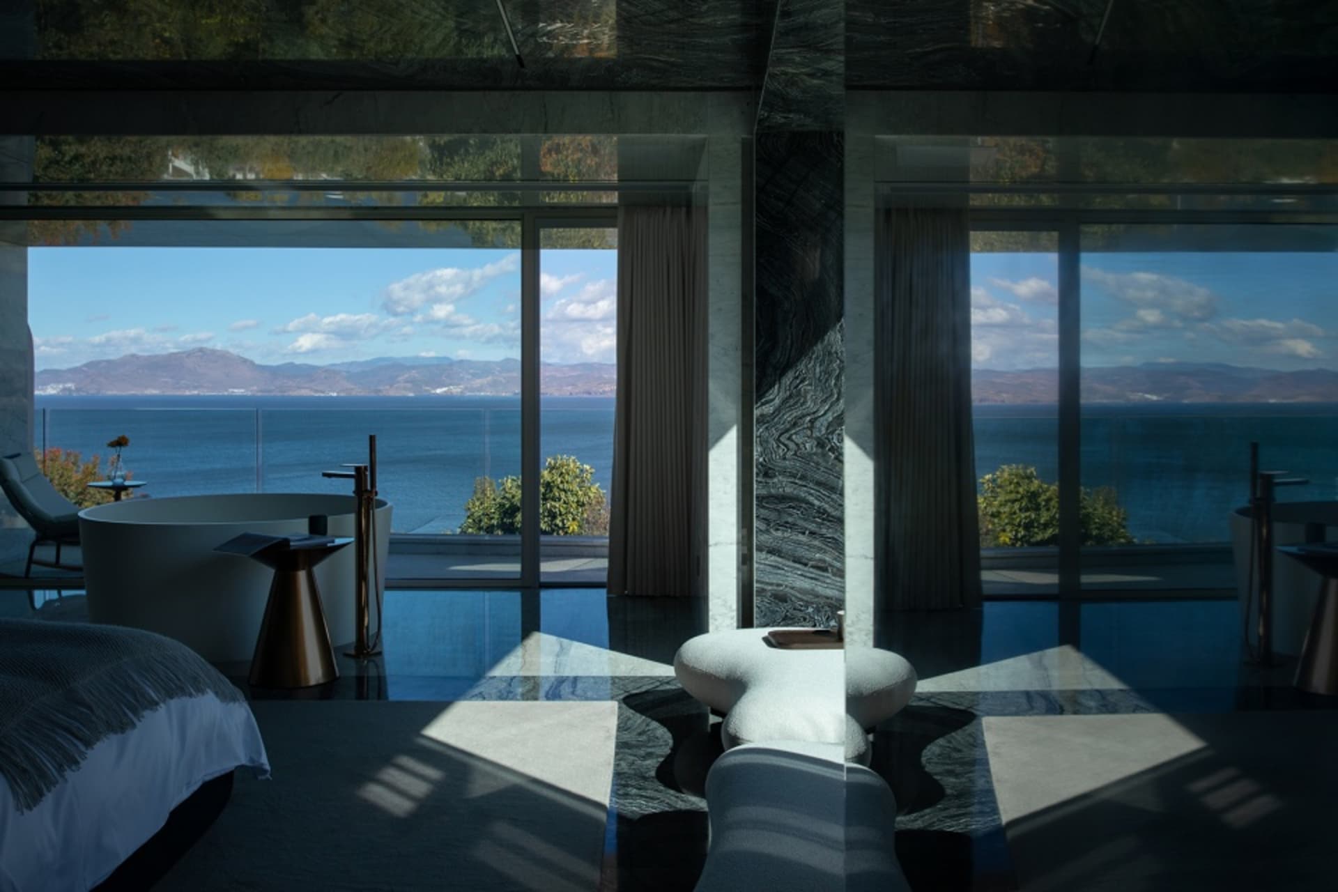 A modern bedroom featuring marble and glass materials with a stunning sea view.