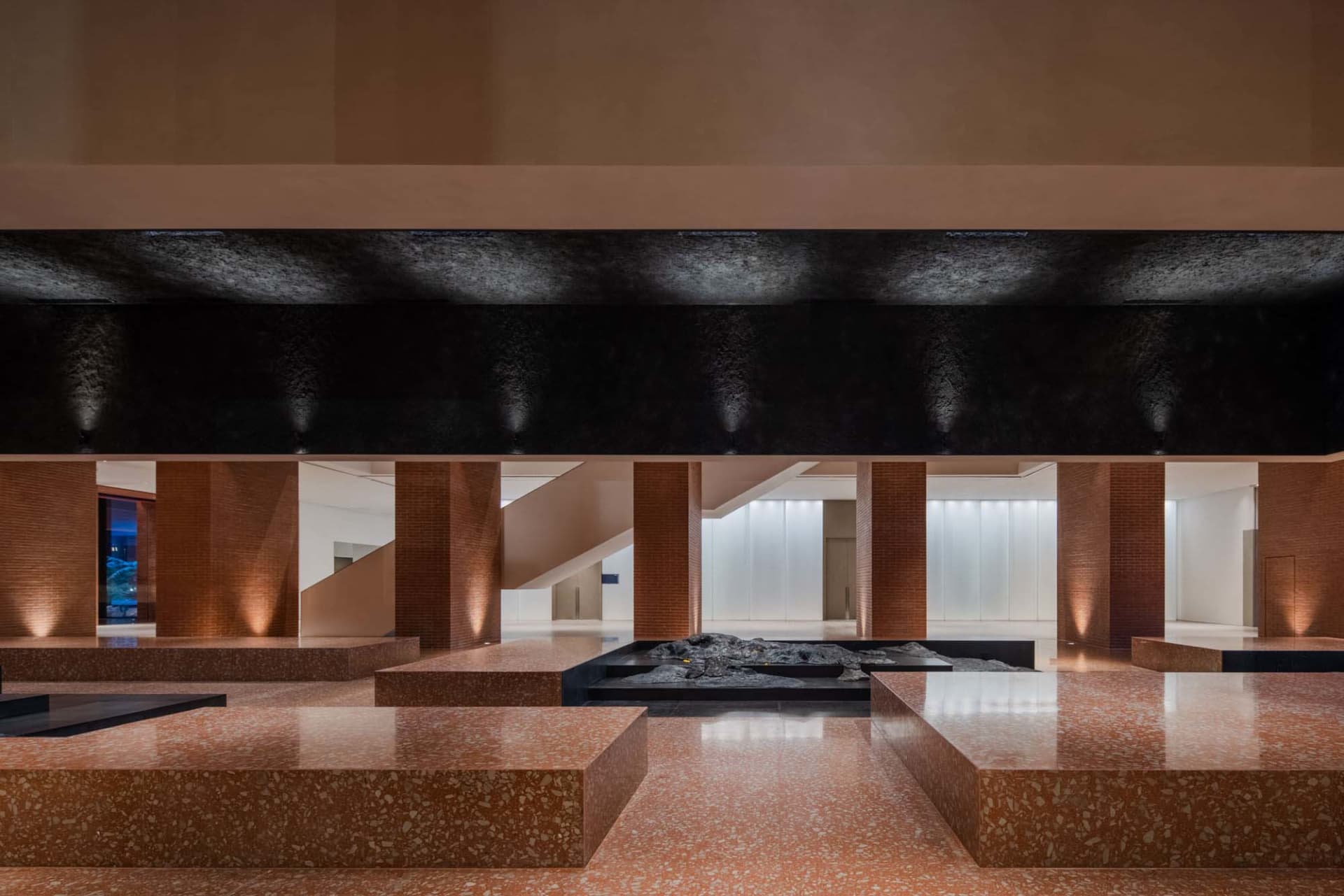 An elegant modern lobby with concrete columns and flooring, illuminated by soft lighting.
