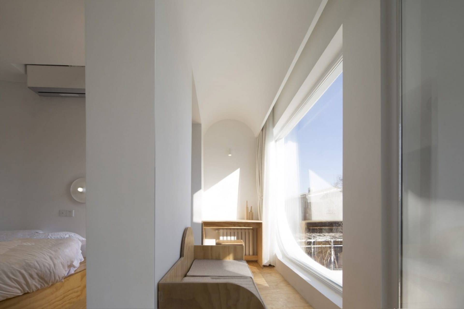 A modern minimalist bedroom with a wooden bench and large window.