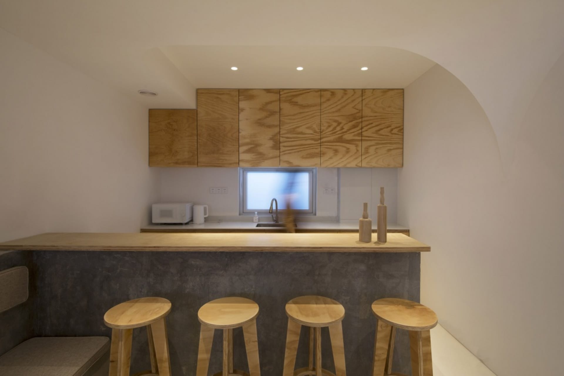 Kitchen area featuring modern minimalist design with wooden cabinets and stools.