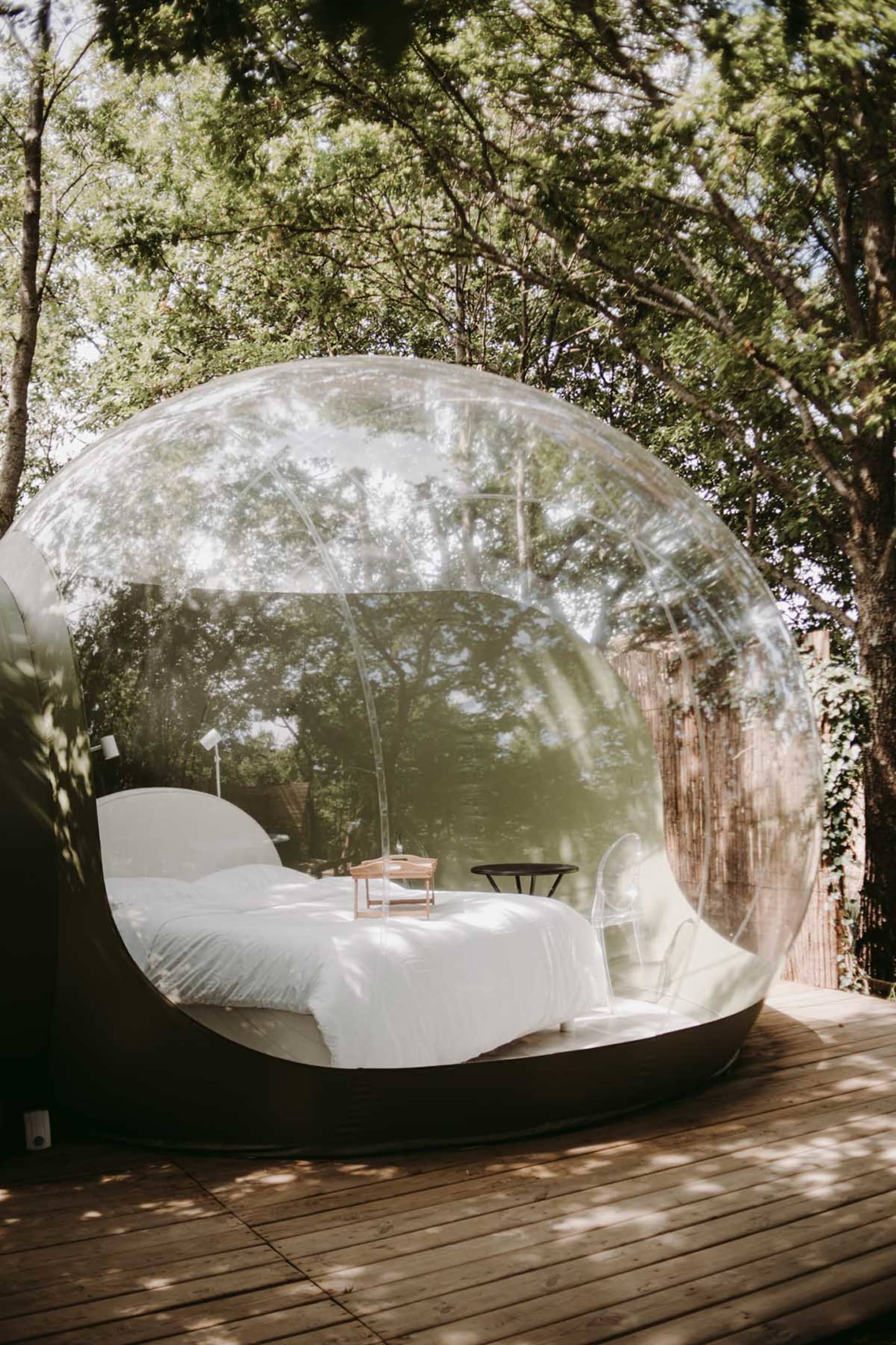 Transparent bubble-shaped outdoor bedroom with a white bed and minimalistic design.