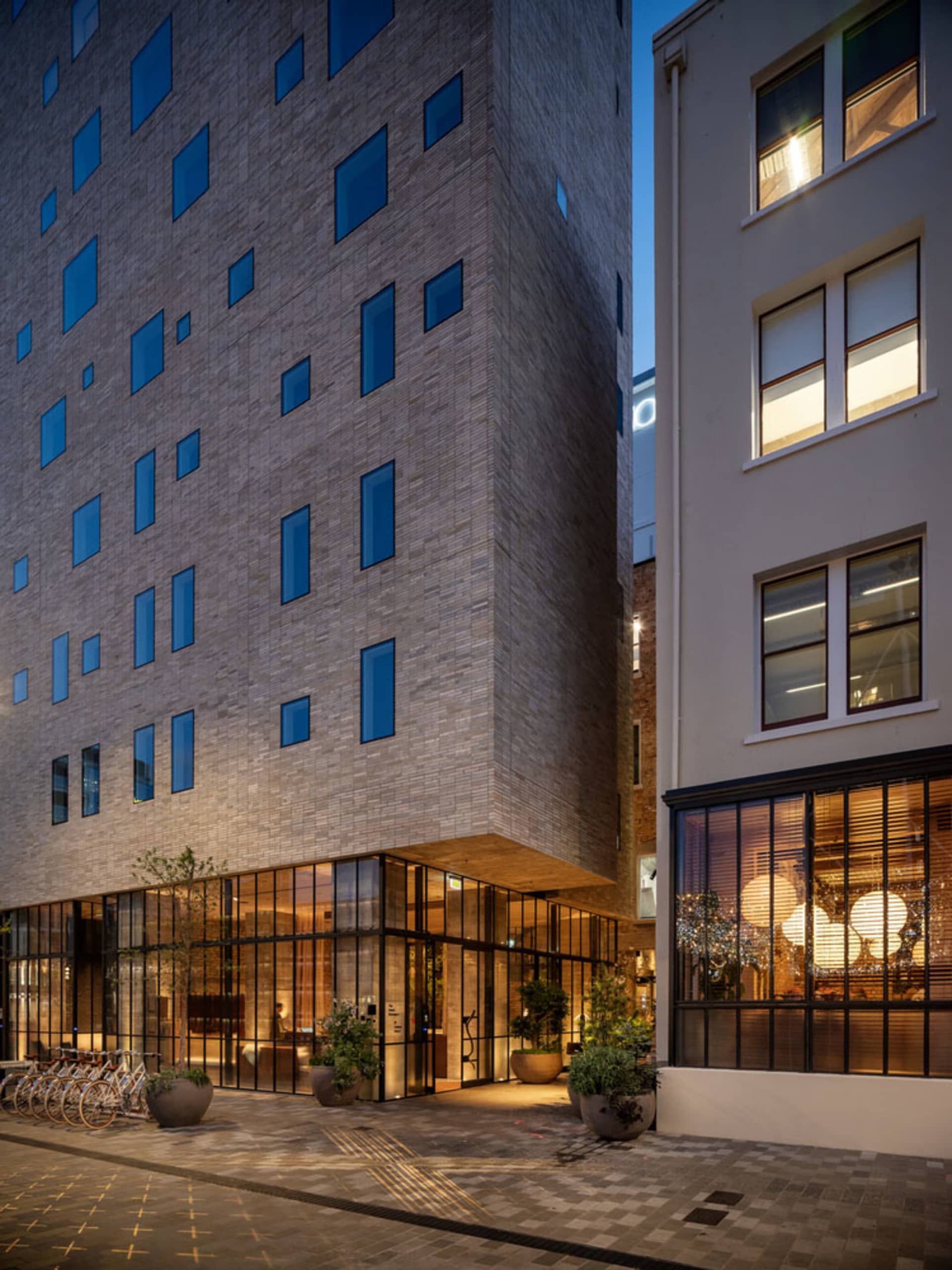Nighttime view of a modern apartment building with concrete and glass facade, featuring numerous windows and a bicycle parkin