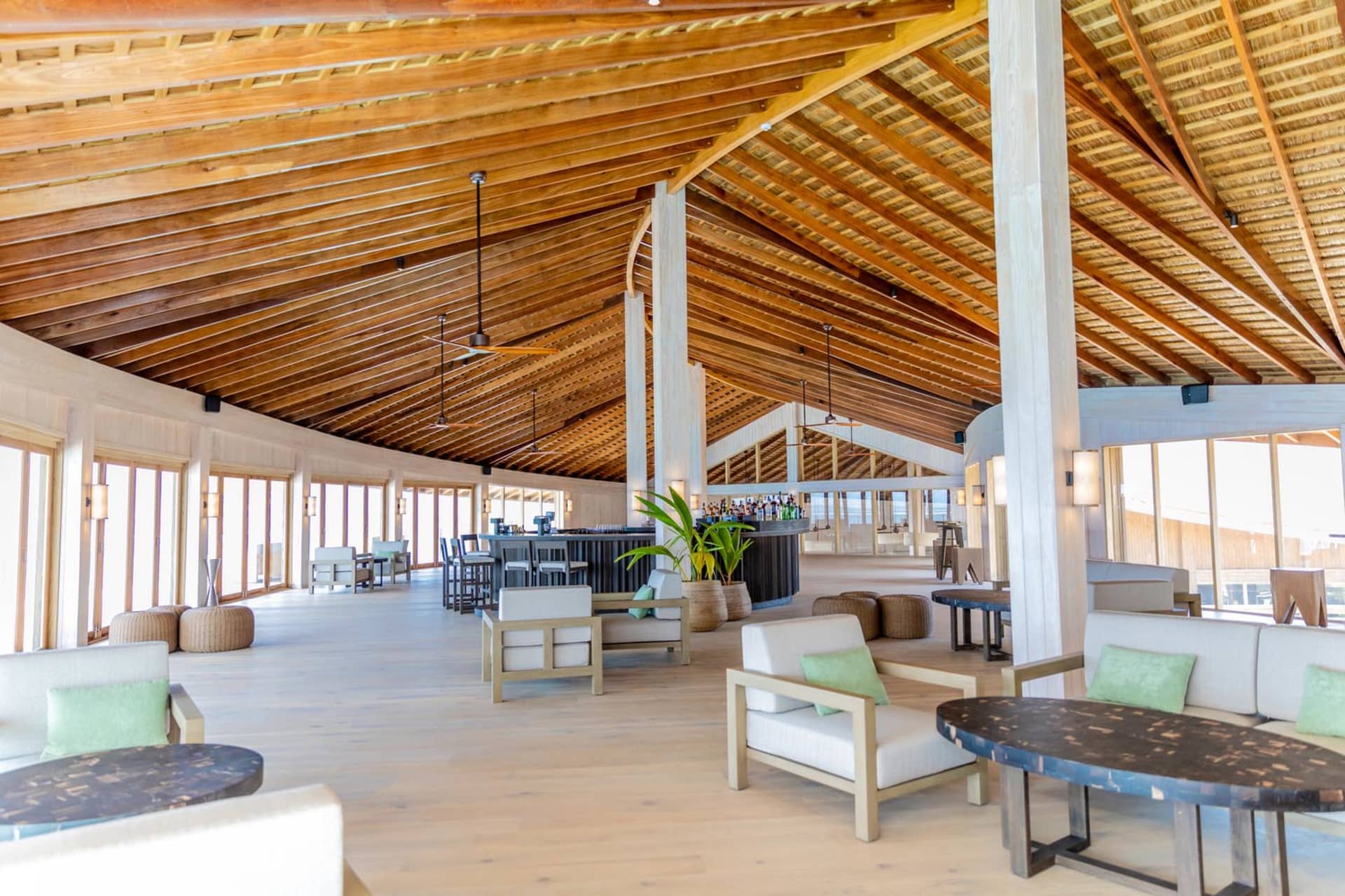 Modern hotel lobby with white and green furniture, wooden ceiling beams, and a bar area.