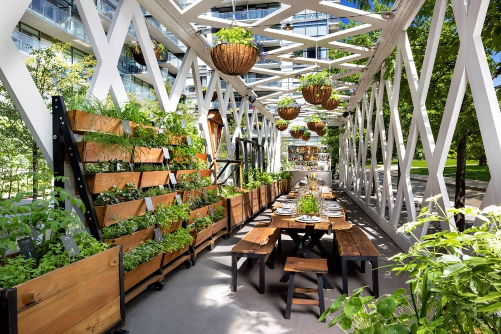 戶外餐廳座位區，木質餐桌搭配懸掛式植栽盆器，充滿綠意，由白色金屬結構支撐