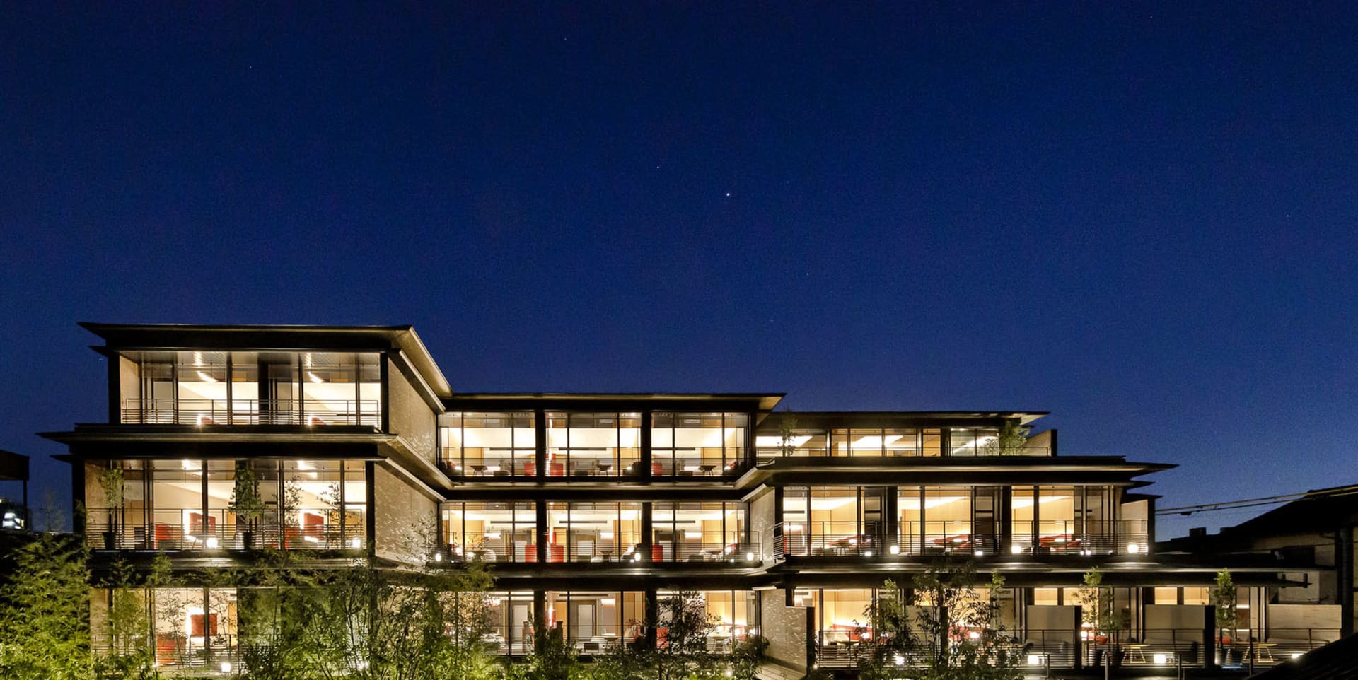 A modern building with a glass exterior illuminated at night, with a clear sky above.