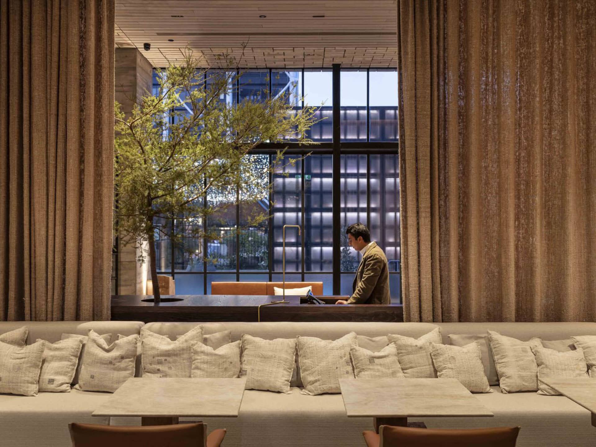 A modern restaurant interior with a long bench, leather couches, and fabric curtains.