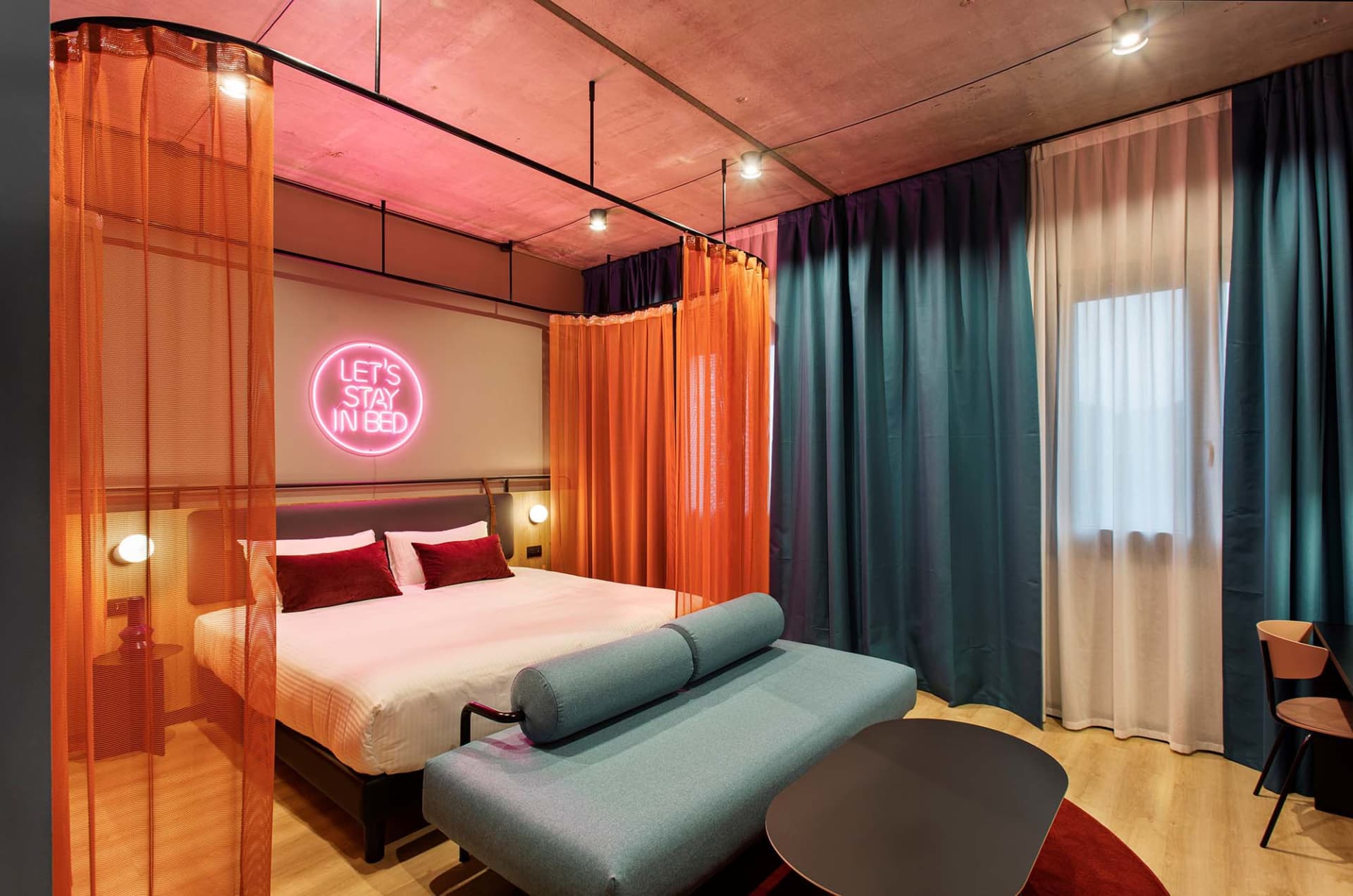 現代酒店客房，設有臥床、窗簾，以及寫著「Let's Stay in Bed」的標語。