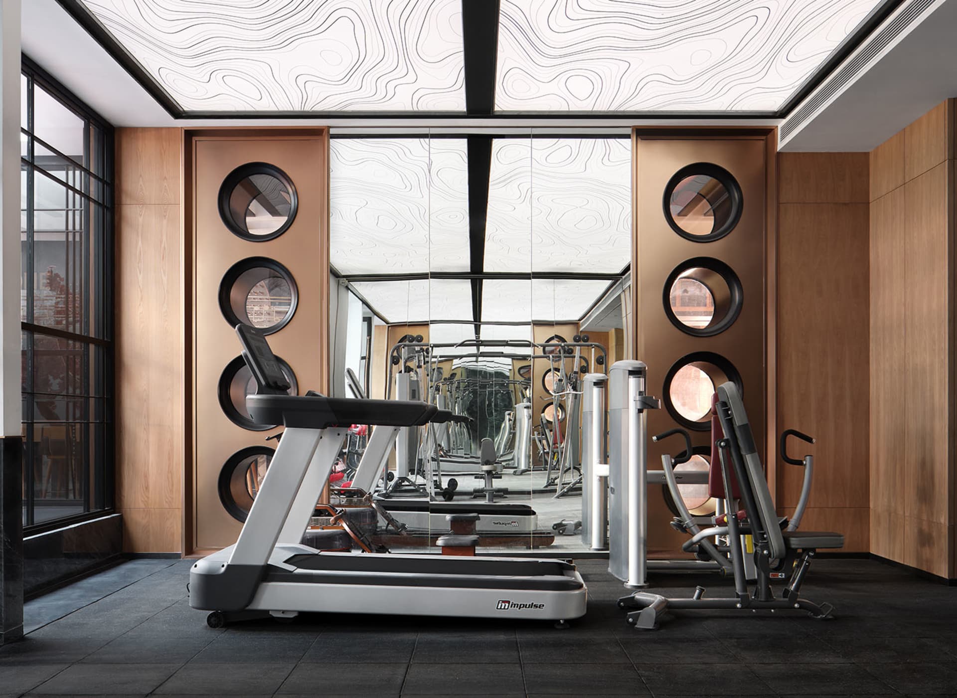 A modern, minimalist commercial gym interior with metallic and glass elements.