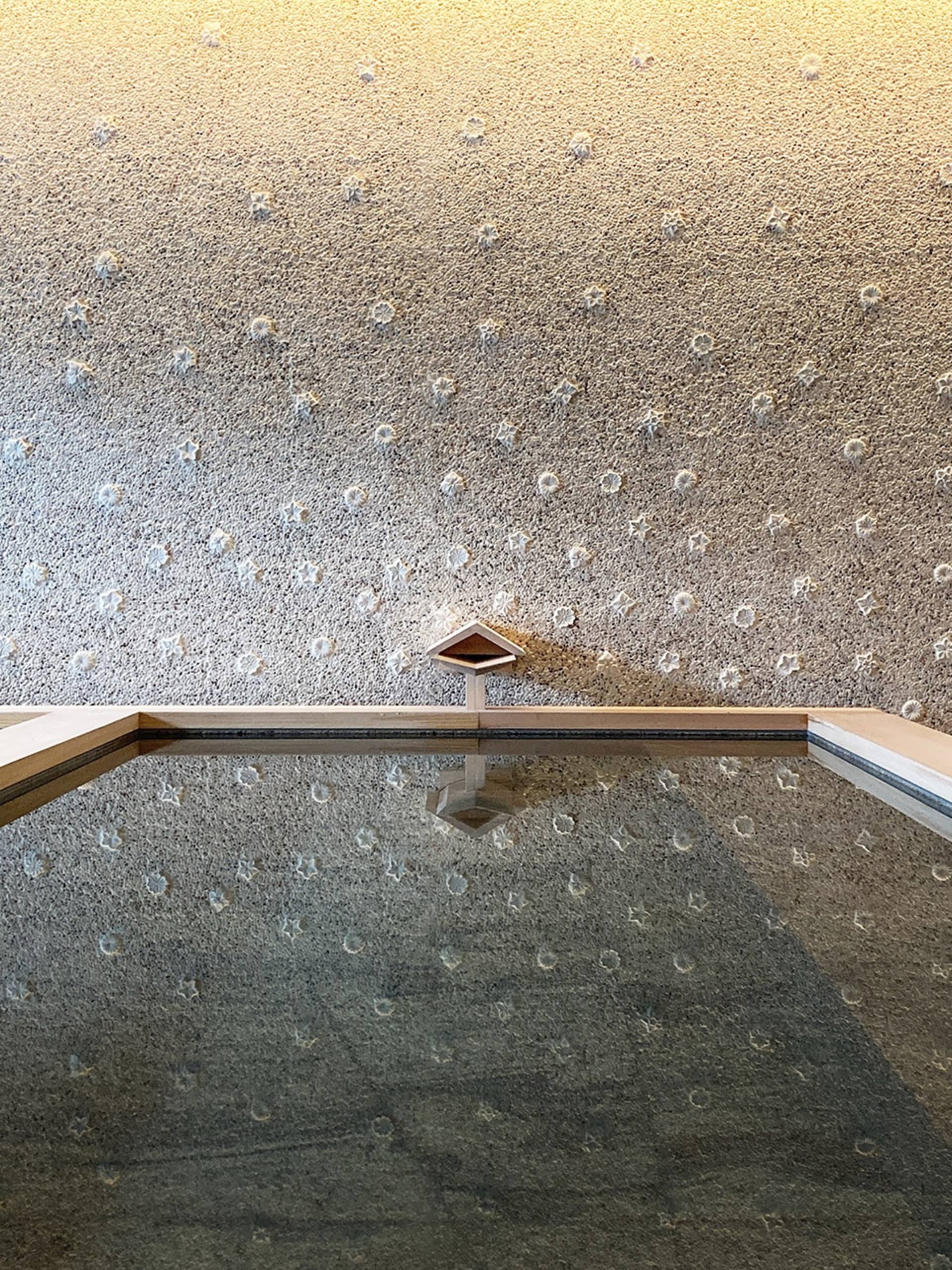 A minimalist pool with a concrete texture and a small wooden structure in the center.