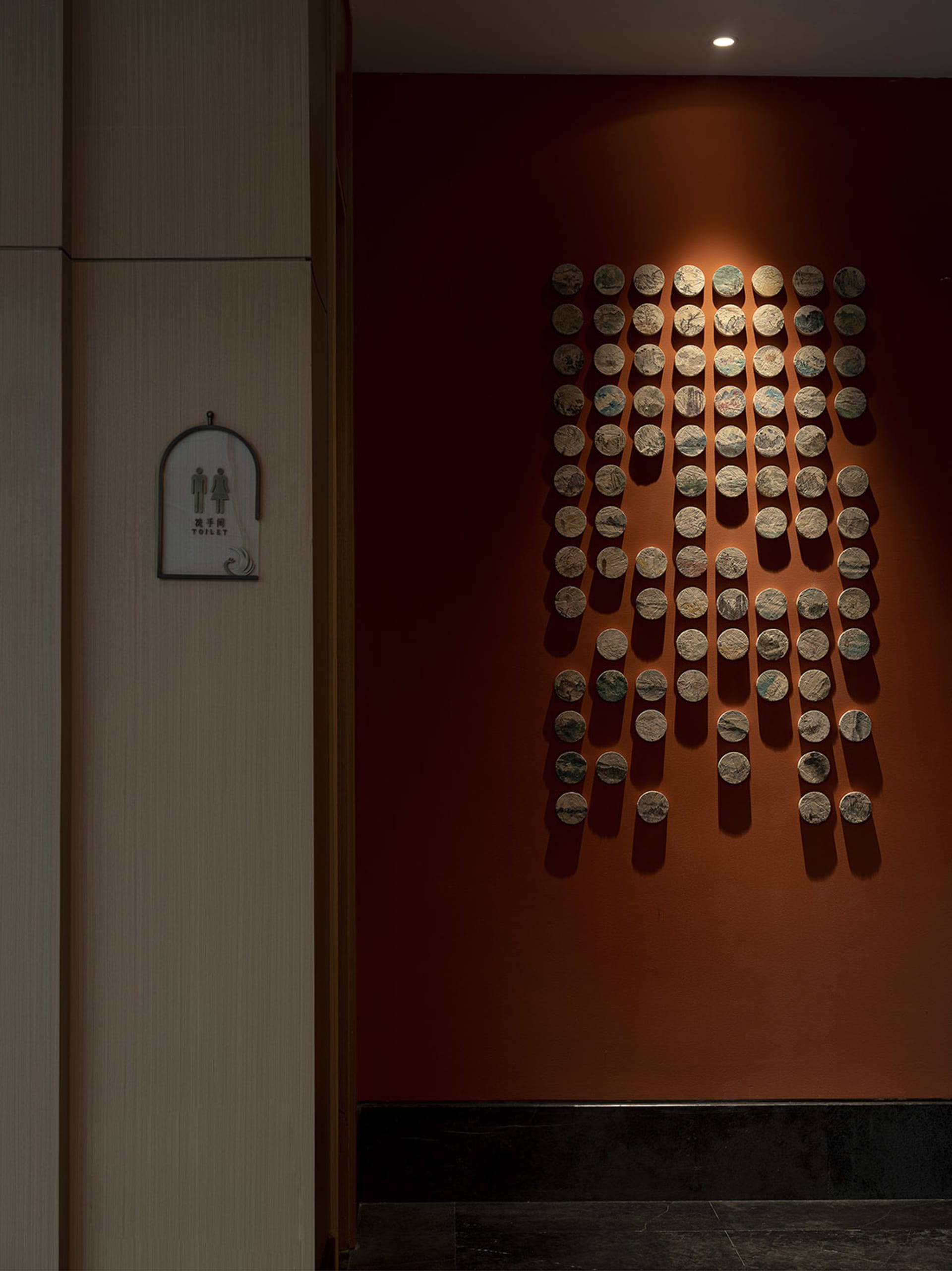 Modern interior space featuring decorative ceramic tiles on a deep red wall, with concrete and terrazzo elements