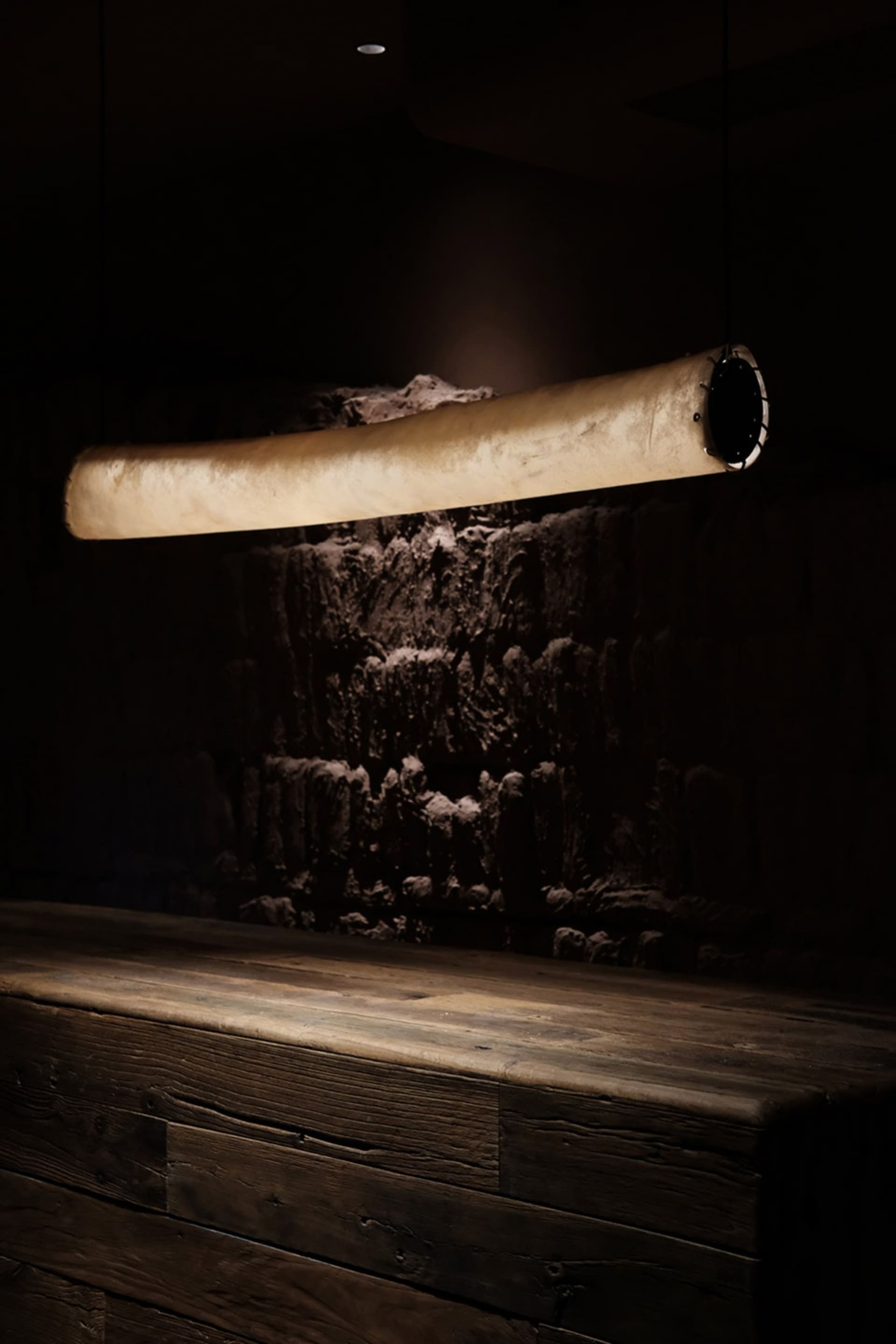 A minimalist concrete bar illuminated by a cylindrical light fixture in a darkened industrial design setting.