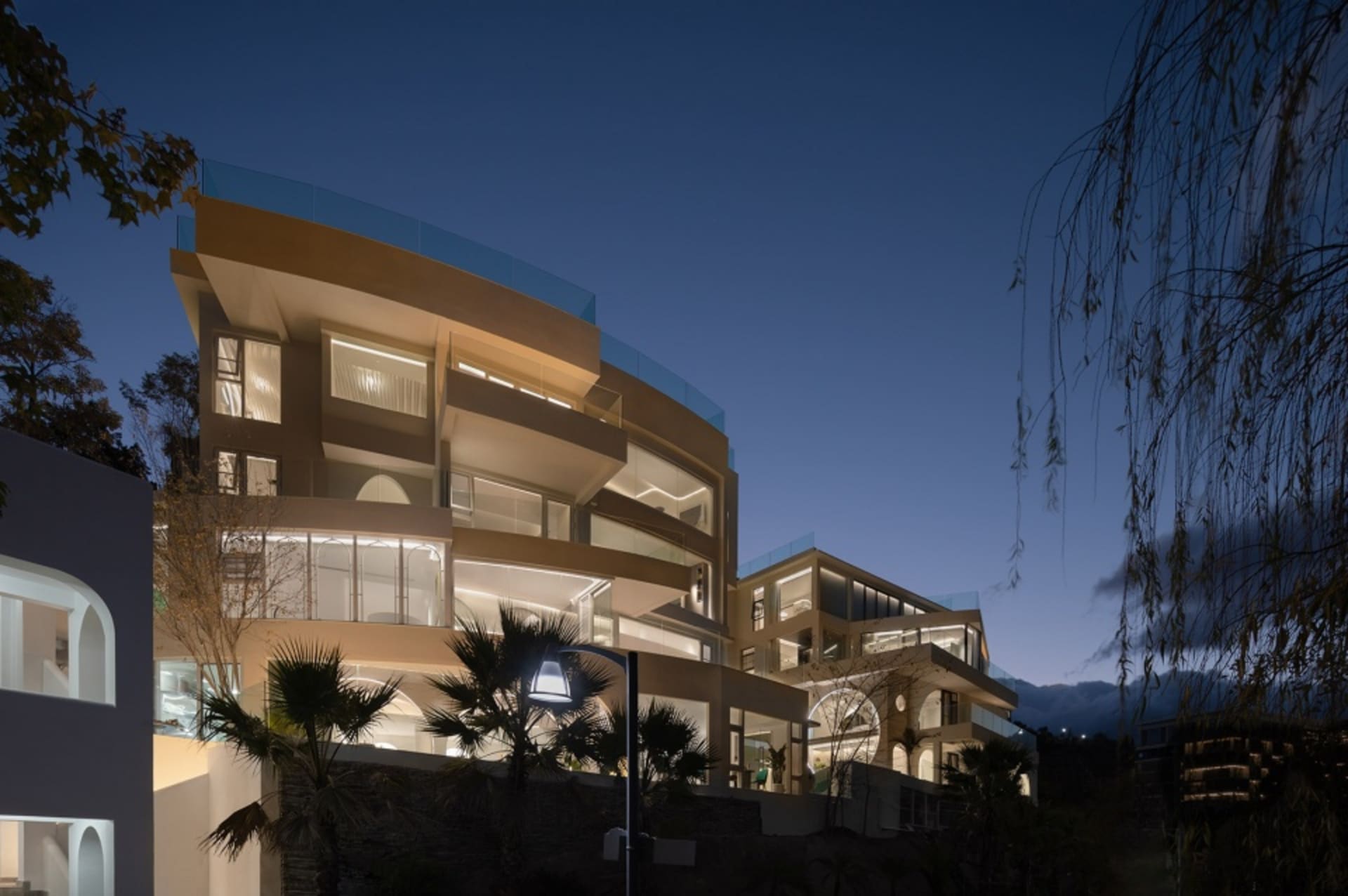 Modern exterior of a building with glass and concrete materials, illuminated at evening.