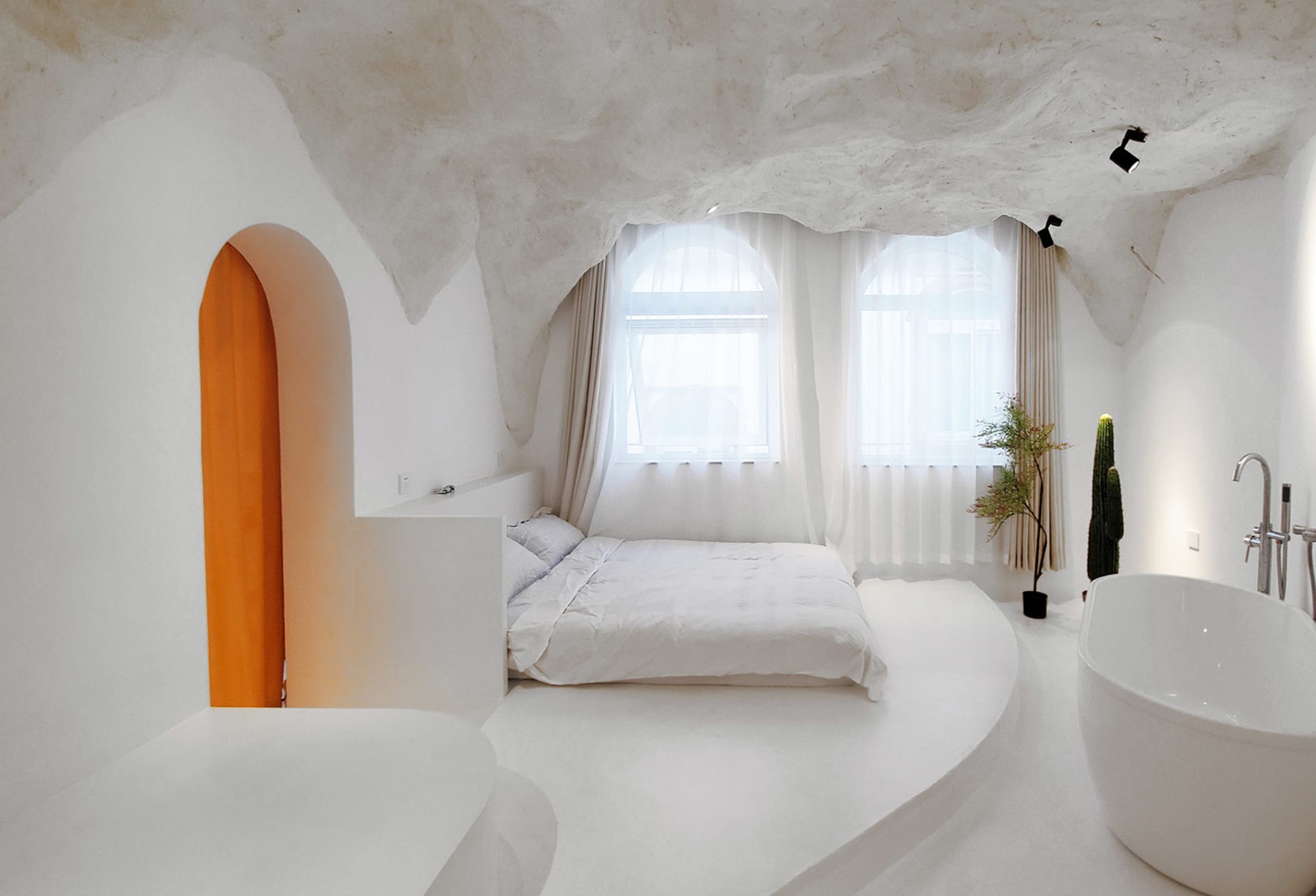 A minimalist bedroom with white walls, concrete ceiling, and floor, featuring a bed with white bedding and a bathtub near the