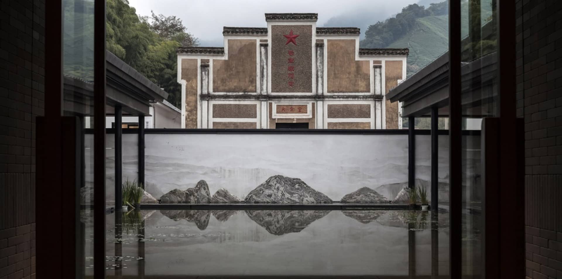 A modern lobby with concrete flooring and walls, featuring a water feature with rocks and a traditional Chinese architectural