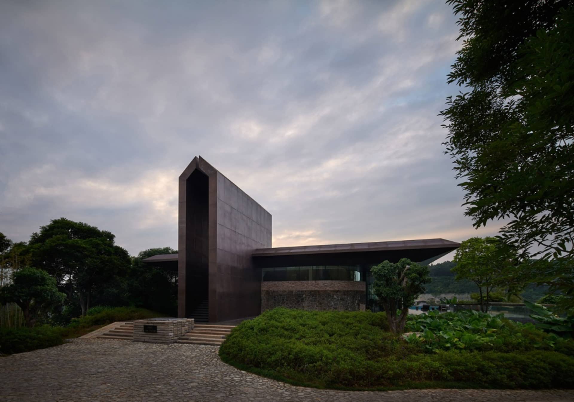 一座現代住宅擁有金屬與玻璃外牆，周圍環繞綠意並設有石板步道。
