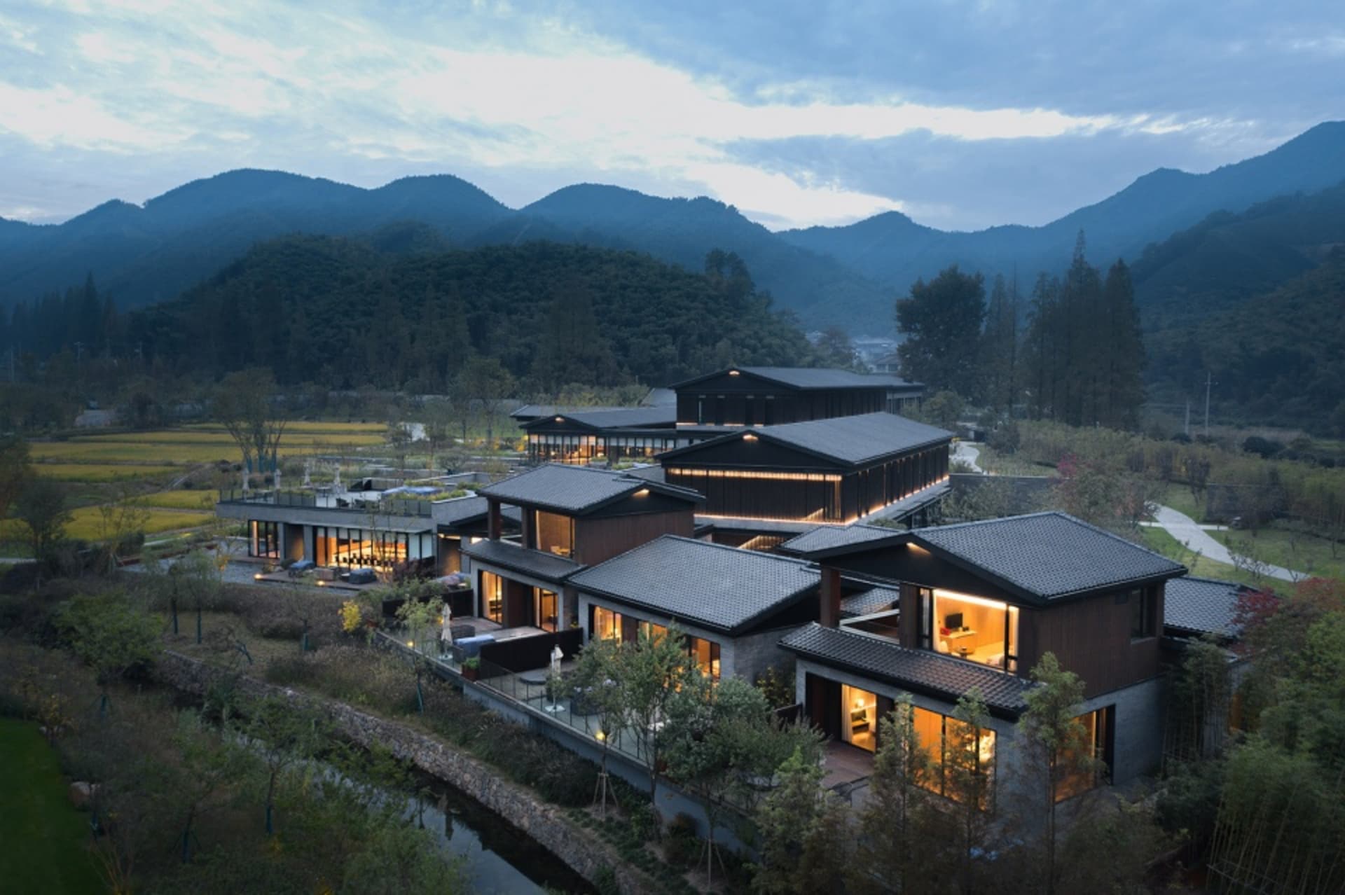 一座現代住宅度假屋,以磚牆與混凝土結構為主,環繞著茂密綠意,背倚山景。