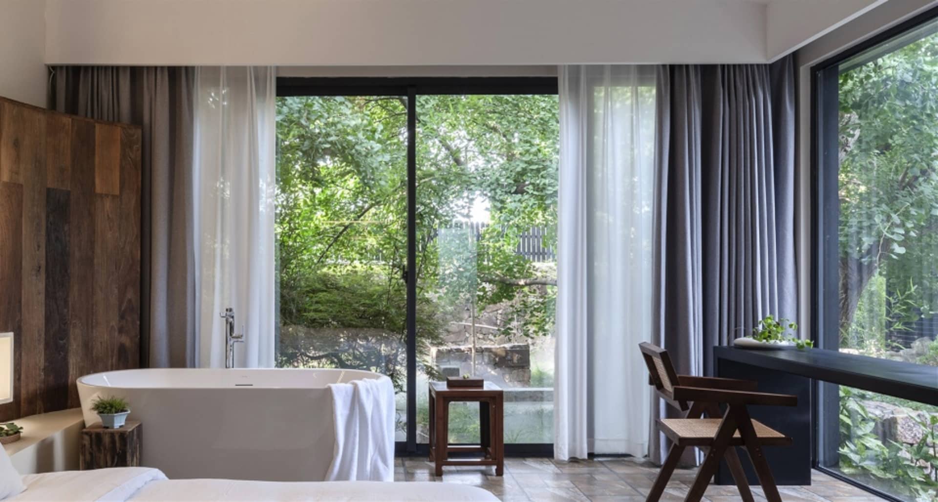 A modern bathroom featuring a freestanding bathtub wrapped in a white towel, a wooden floor, and large windows with white and