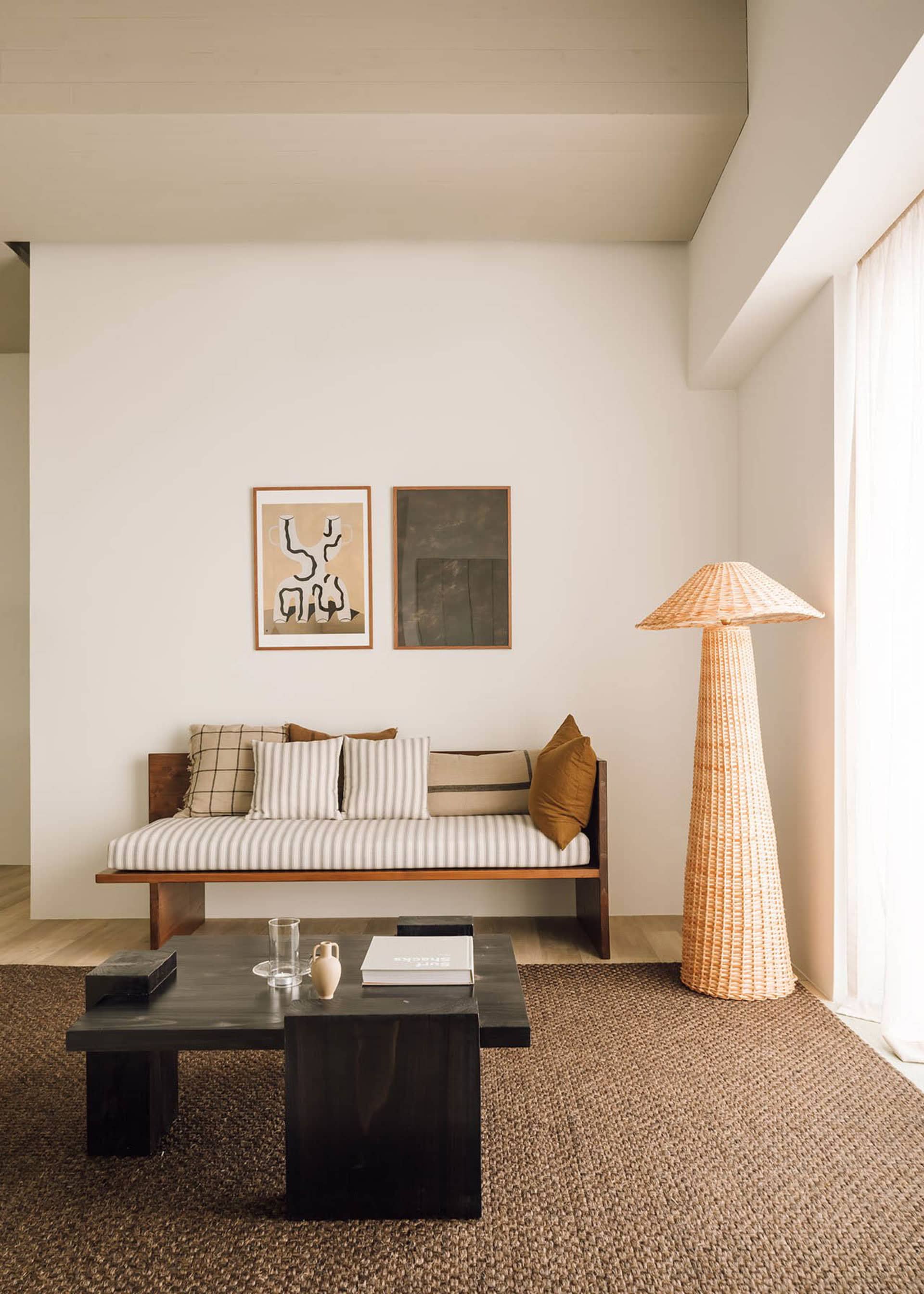 A modern living room featuring a wooden sofa, woven-fiber floor lamp, and abstract wall art.