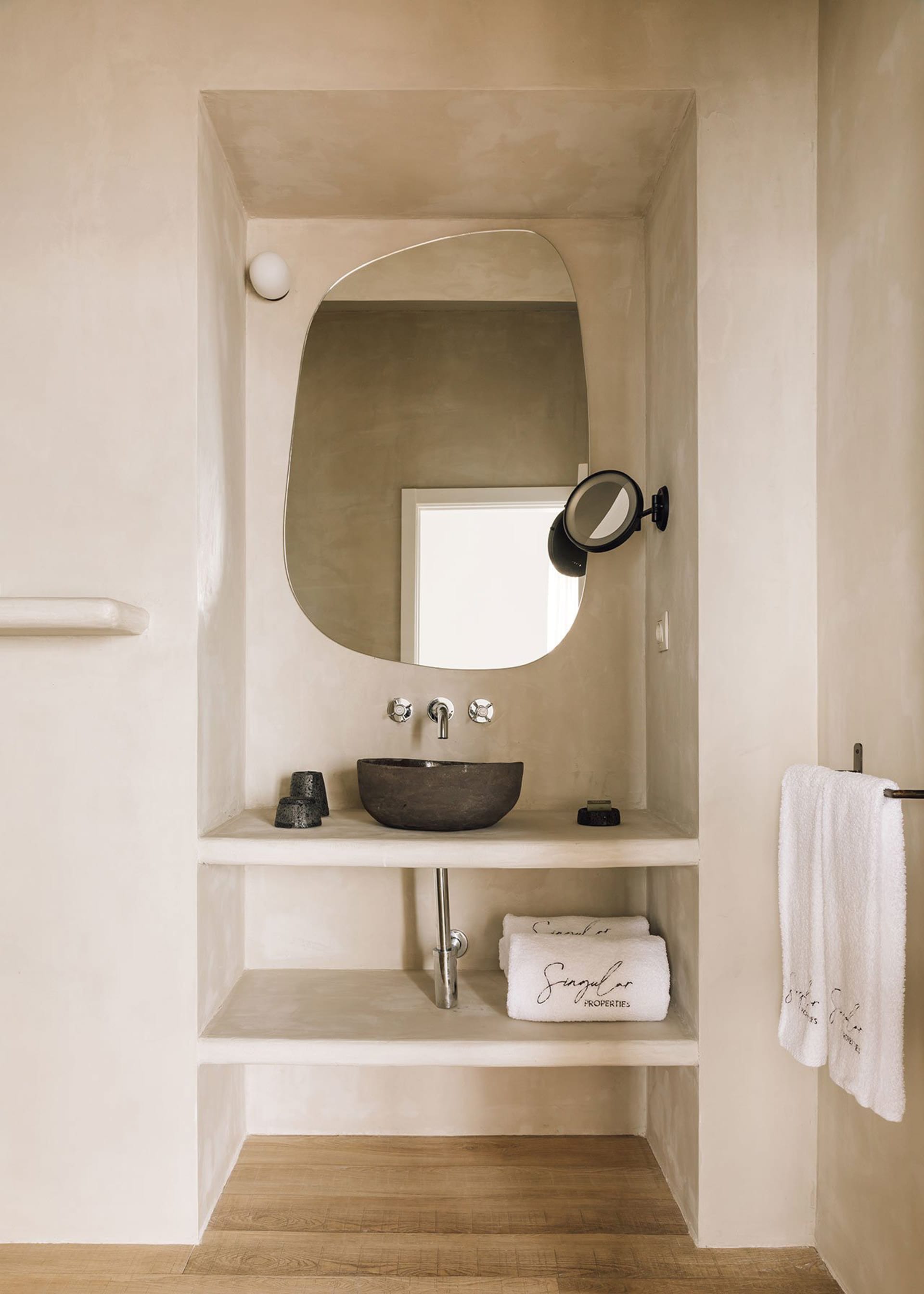 A minimalist bathroom with a concrete sink, wall-mounted faucet, and a round mirror above it. The space is adorned with white