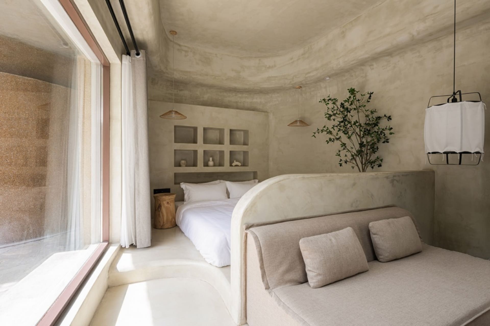 A minimalist bedroom with concrete walls, a large bed, and a grey sofa.
