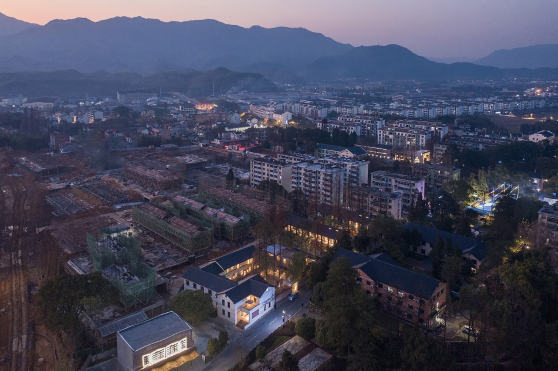 現代城市在黃昏時分，建築物燈火通明，背景有山巒。