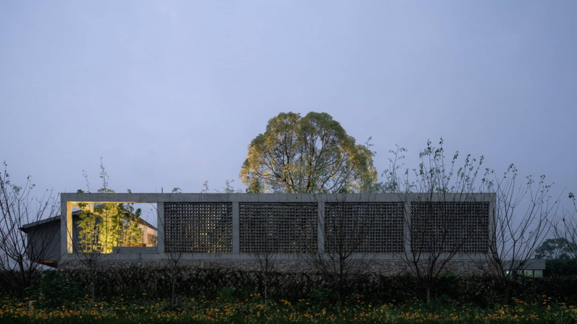 A modern concrete structure with a lattice facade, surrounded by trees and flowers.
