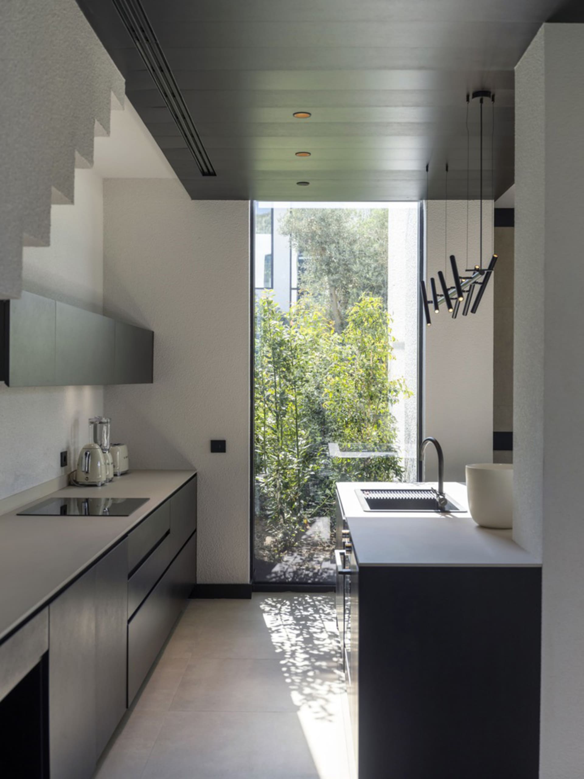 Modern minimalist kitchen with sleek black cabinetry and a large window overlooking greenery.