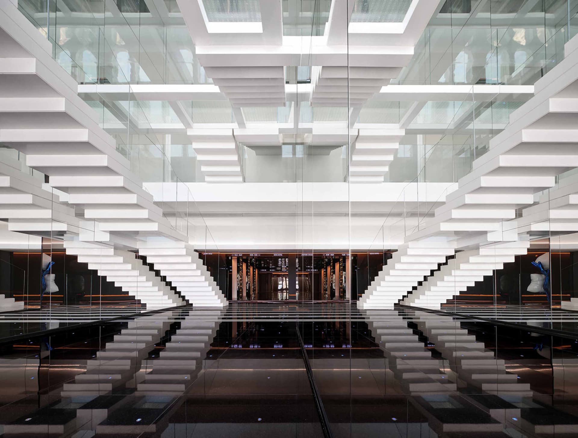 A modern office lobby with glass staircases and a reflective floor.