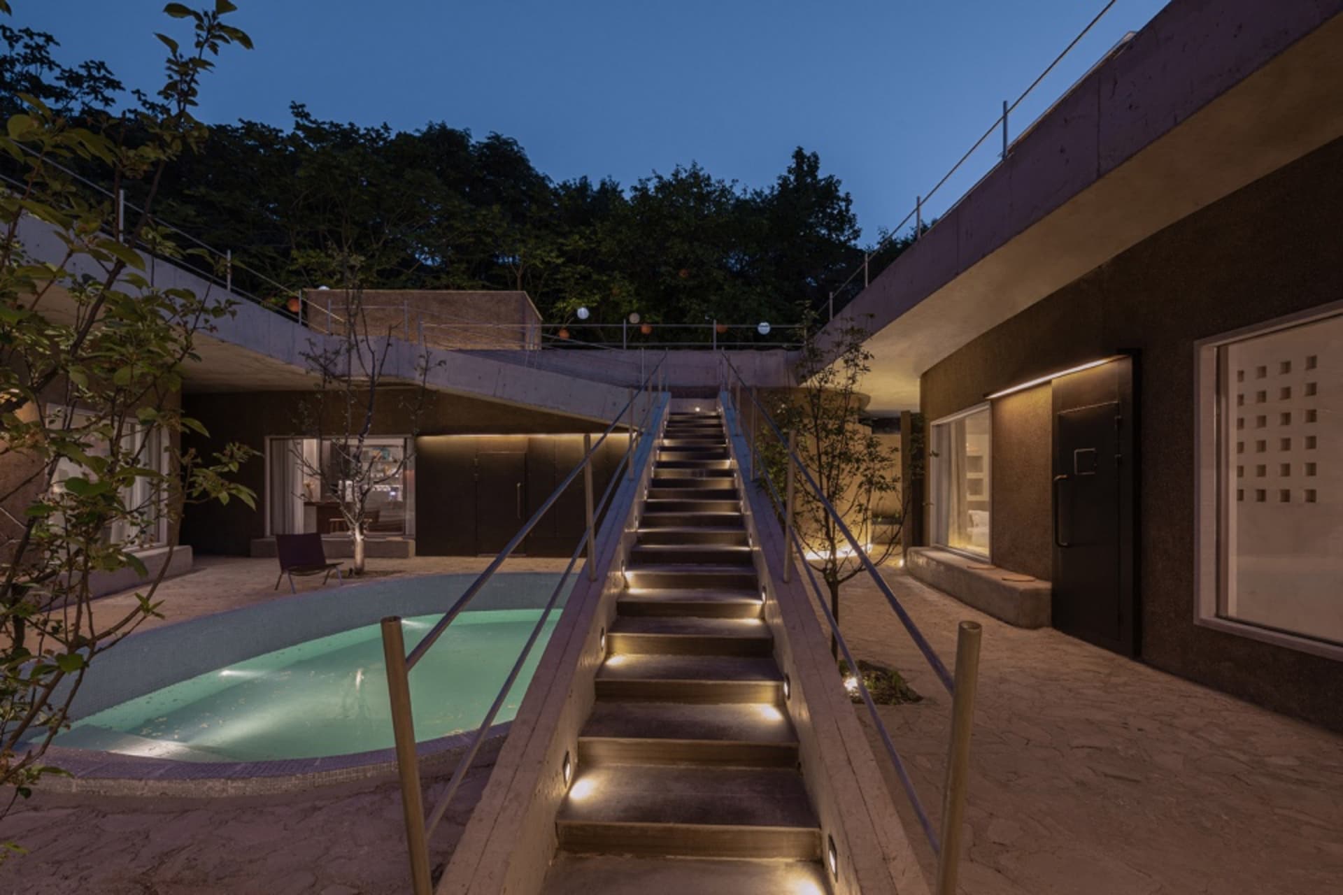 混凝土樓梯通往現代住宅建築，夜景中可見泳池與樹木。