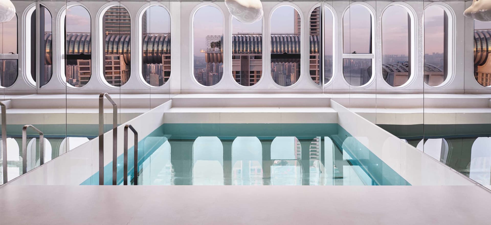 Modern rooftop swimming pool enclosed by a glass fence overlooking a cityscape.