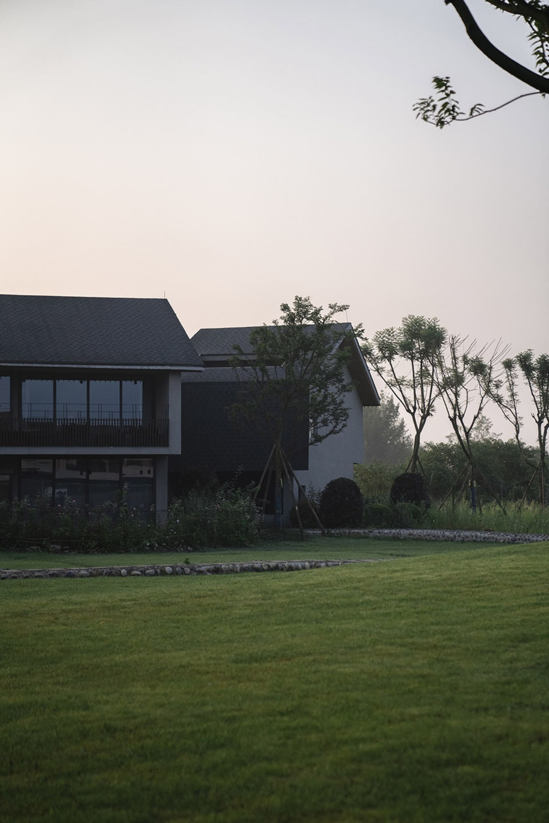 A modern house with concrete and glass exterior surrounded by greenery.