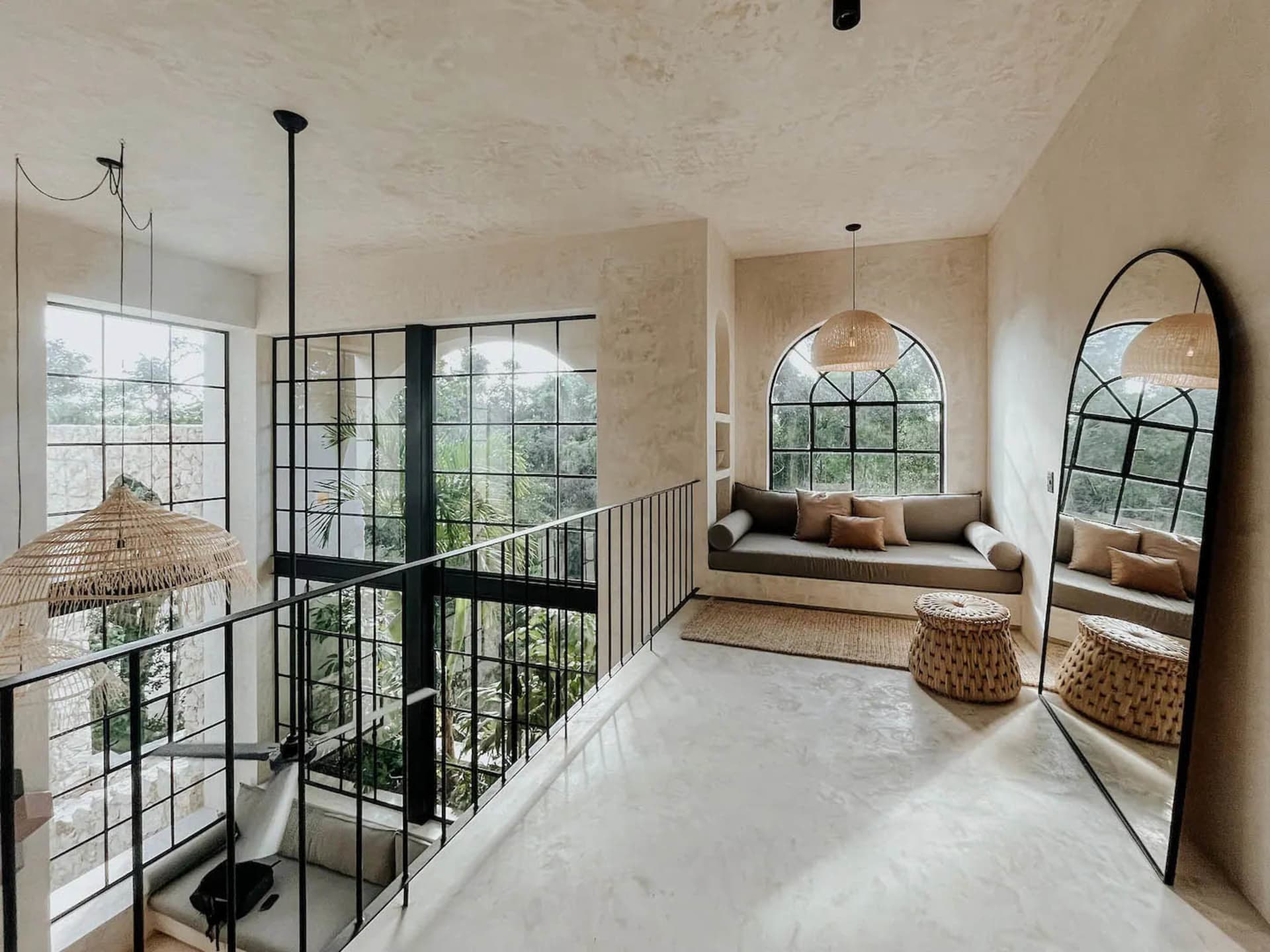 A modern living room with concrete walls, arched windows, and rattan furniture.