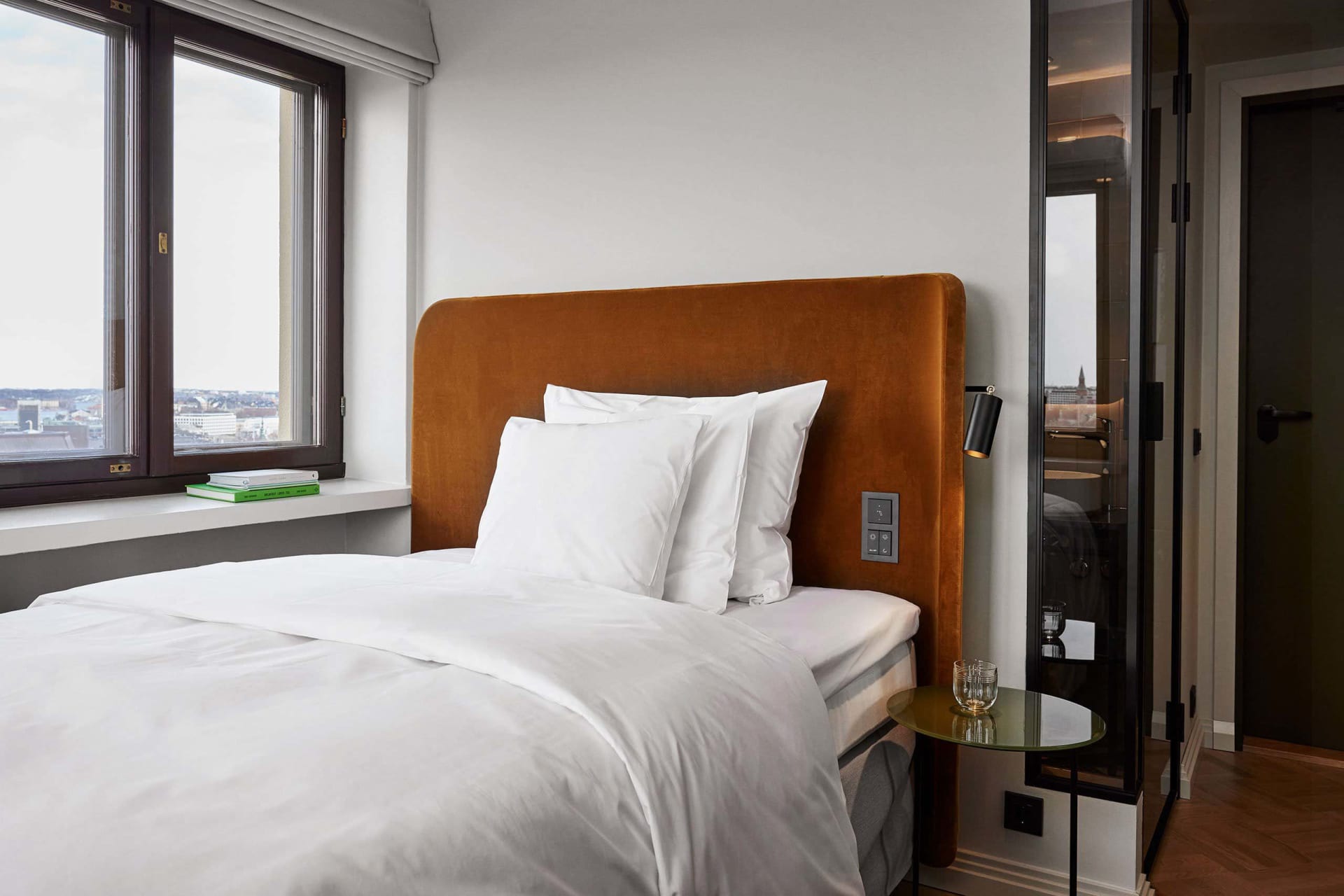 A modern, minimalist bedroom with a single bed, white bedding, and a brown upholstered headboard.