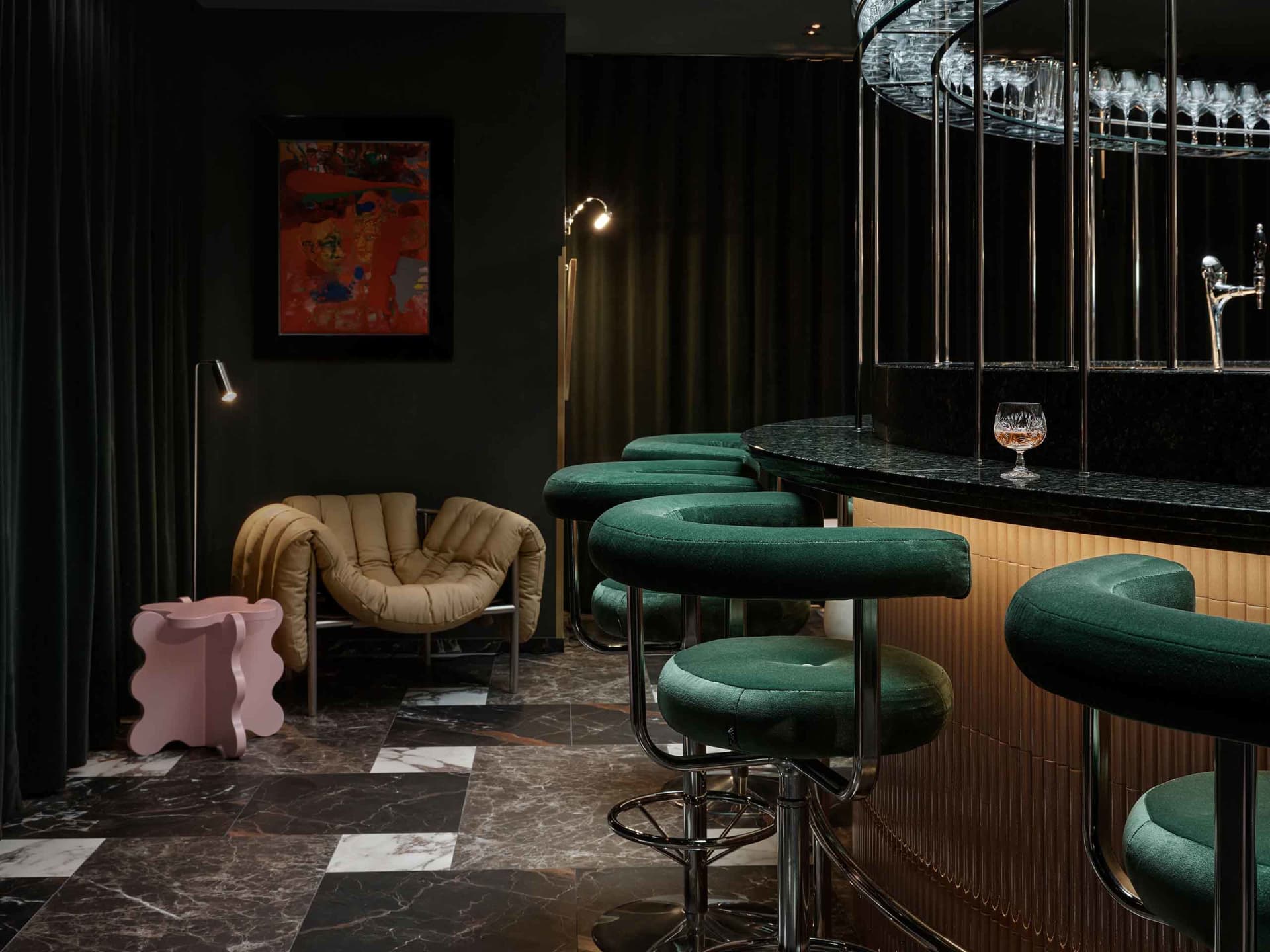 Modern restaurant bar area featuring velvet stools, marble flooring, and metal bar counter.