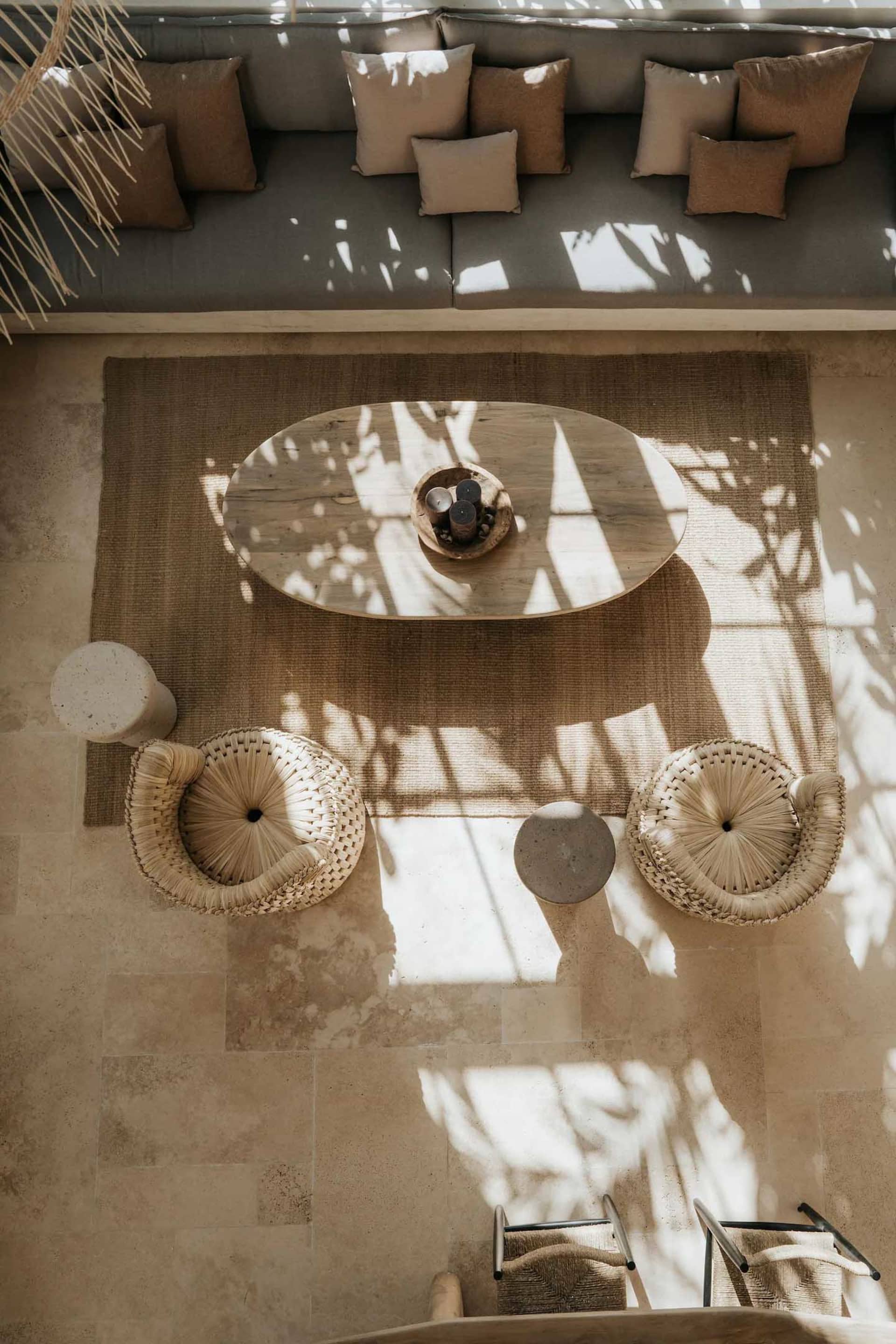 A living room with wicker furniture and woven baskets, featuring a round wooden table and a large sofa adorned with cushions.