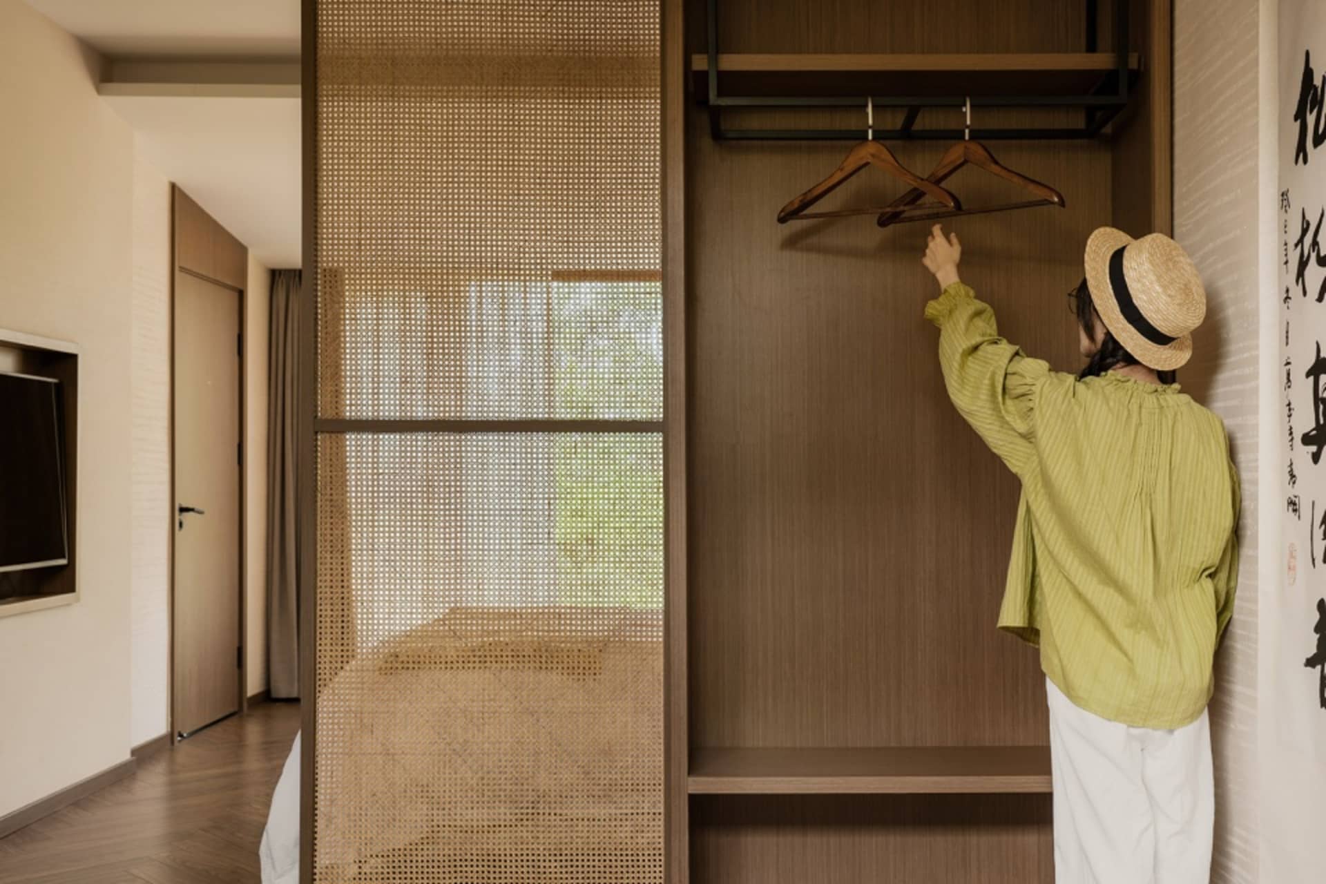 A person wearing a straw hat interacting with an empty wooden wardrobe.