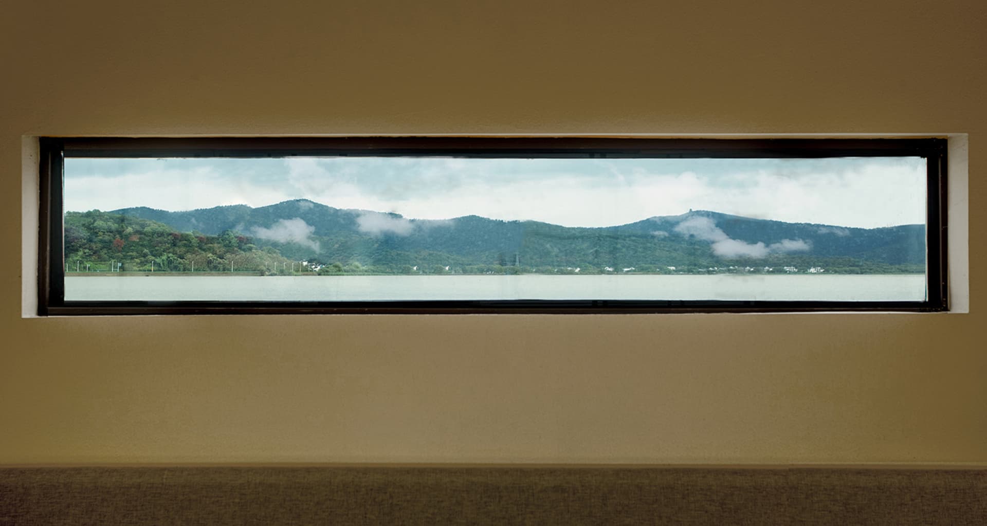 A rectangular window overlooking a serene lake surrounded by mountains and clouds in the background.