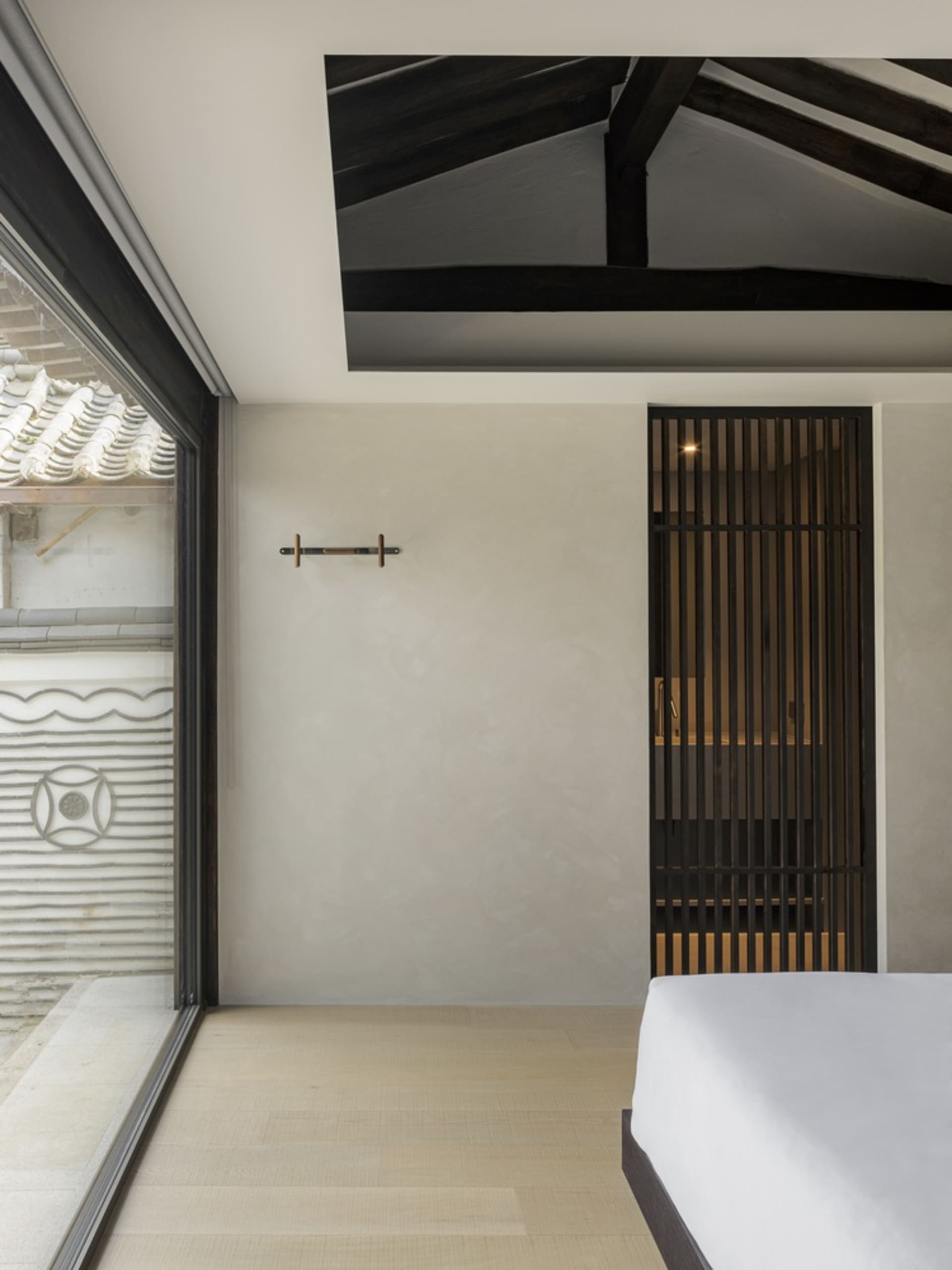 A minimalist bedroom with wooden flooring, a bed, and a simple white wall with a wooden door.
